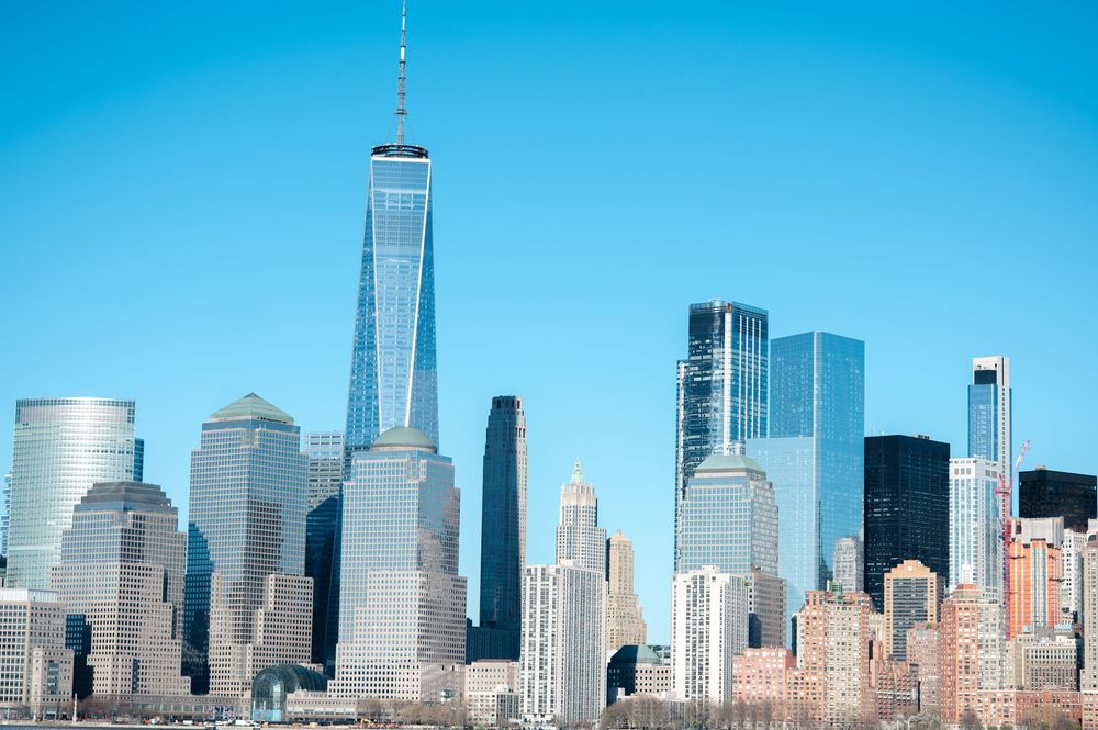 Manhattan skyline featuring One World Trade Center towering over lower Manhattan skyscrapers under a clear blue sky.