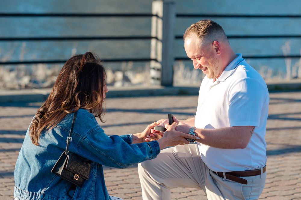 Man kneeling on one knee proposing to woman outdoors, holding ring box in romantic marriage proposal scene.