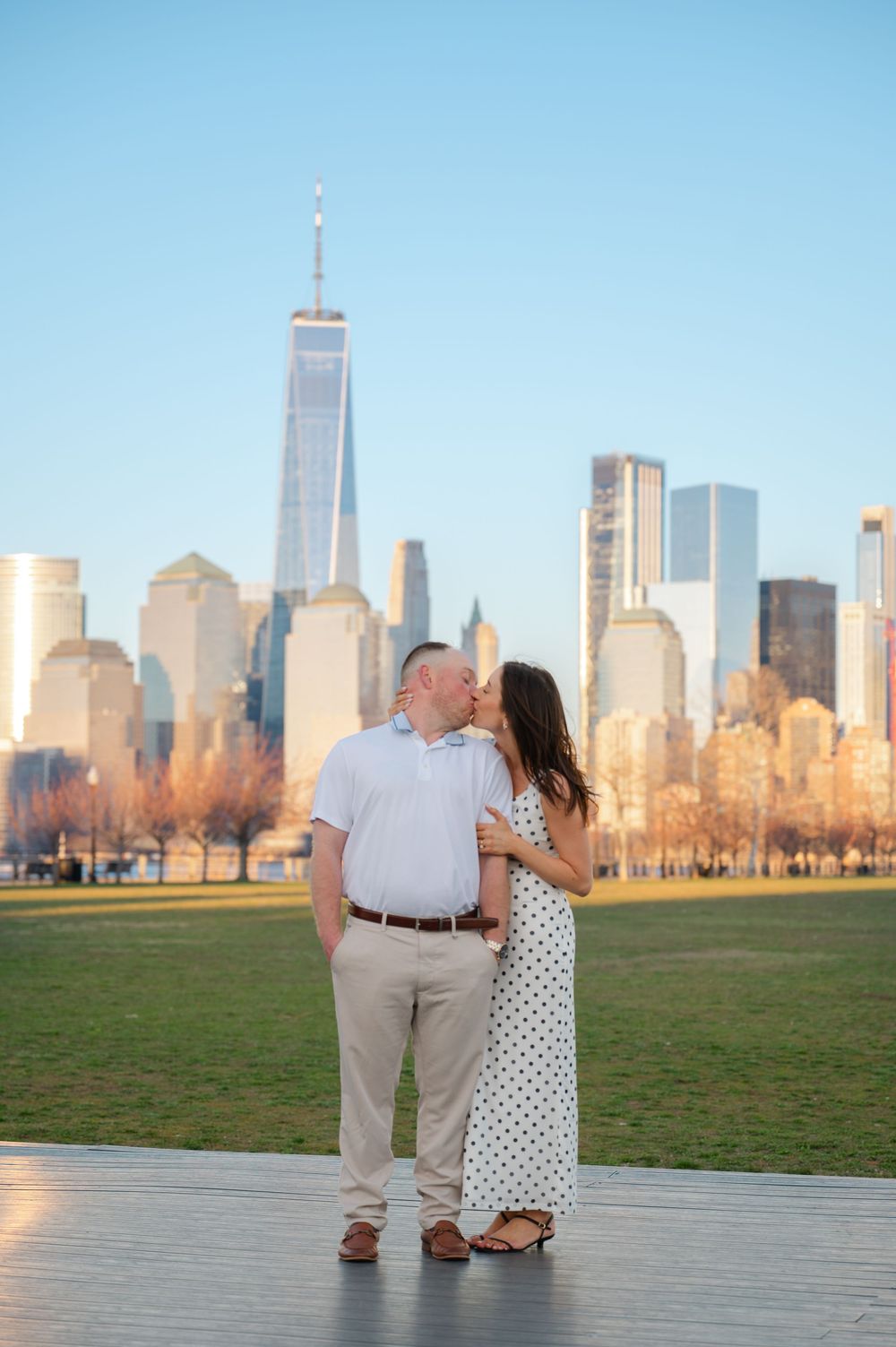 Couple sharing a kiss with One World Trade Center and NYC skyline backdrop at Liberty State Park.