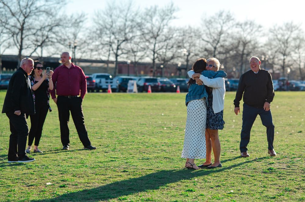 Group of people gathered on a green lawn, with two women embracing in a joyful reunion outdoors.