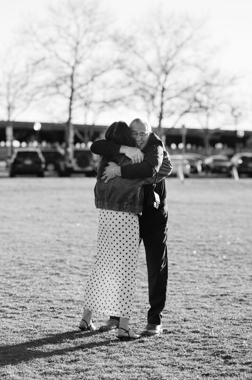 A couple shares a tender embrace in a black and white photo outdoors near bare trees.