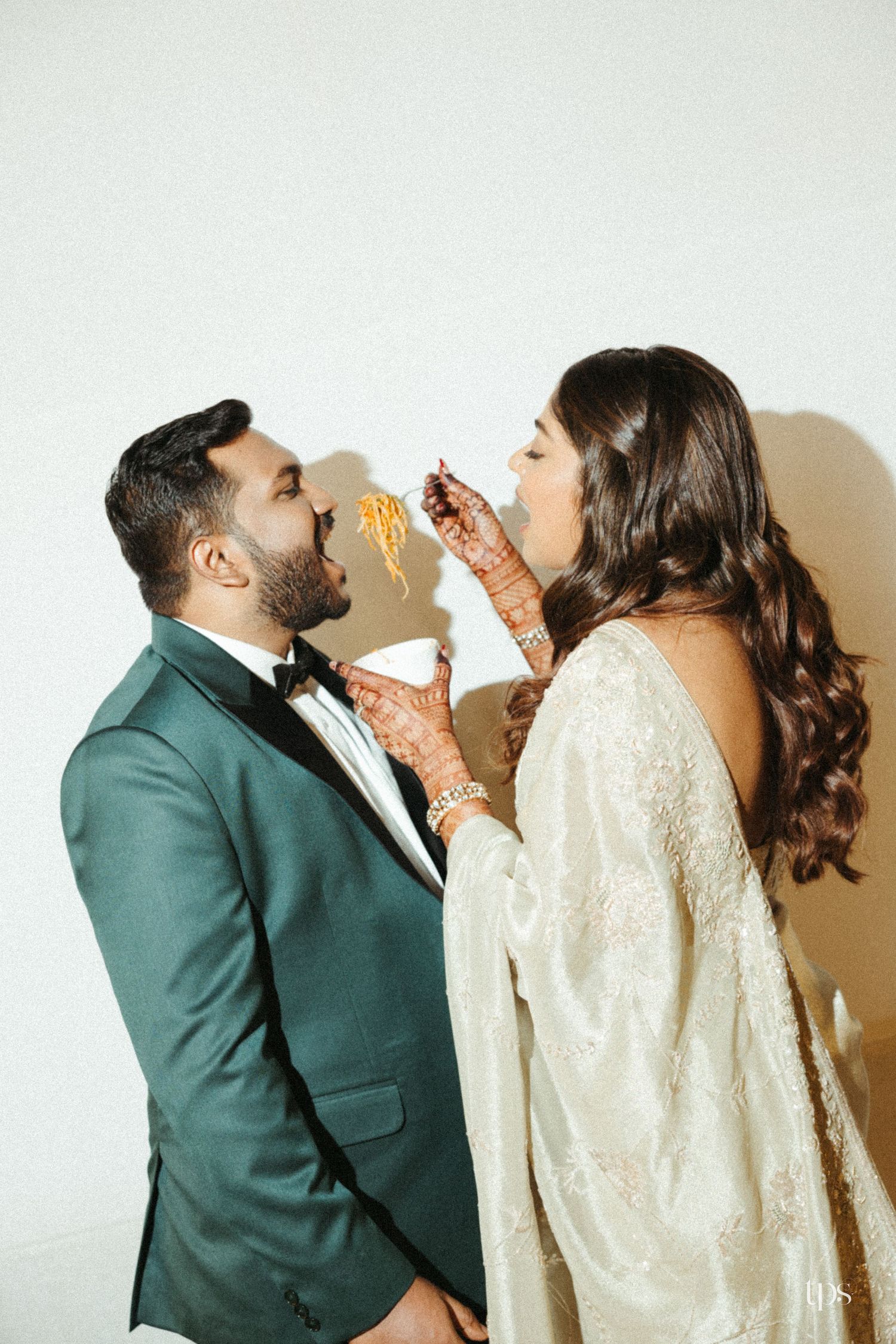Bride in white gown feeds groom in green tuxedo, showcasing mehndi hands captured by a wedding photographer in Sydney, Gold Coast & Brisbane