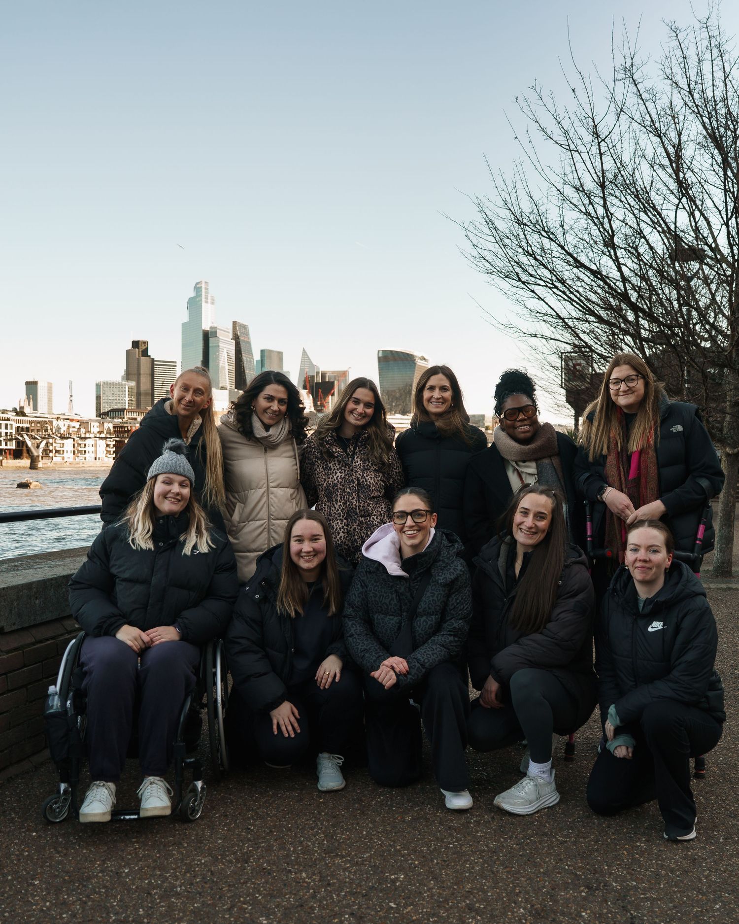 Group of women posing together outdoors with London city skyline in background on a clear winter day.