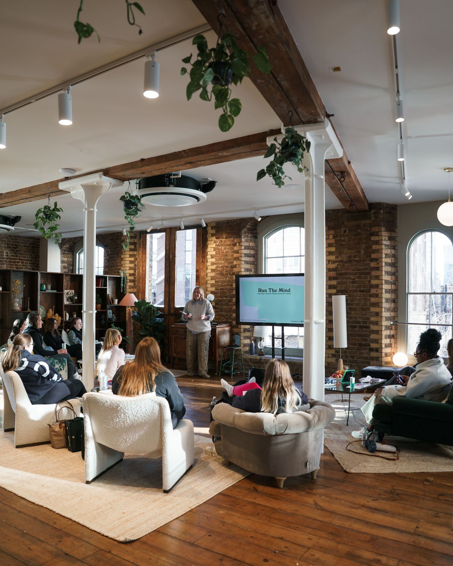 Modern loft event space with exposed brick, hanging plants, and attendees seated watching a presentation.