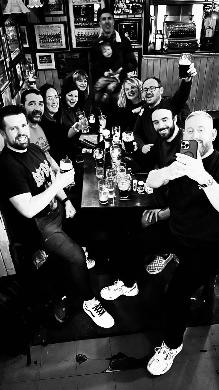 Group of friends enjoying drinks at a pub table in a lively black and white photo.