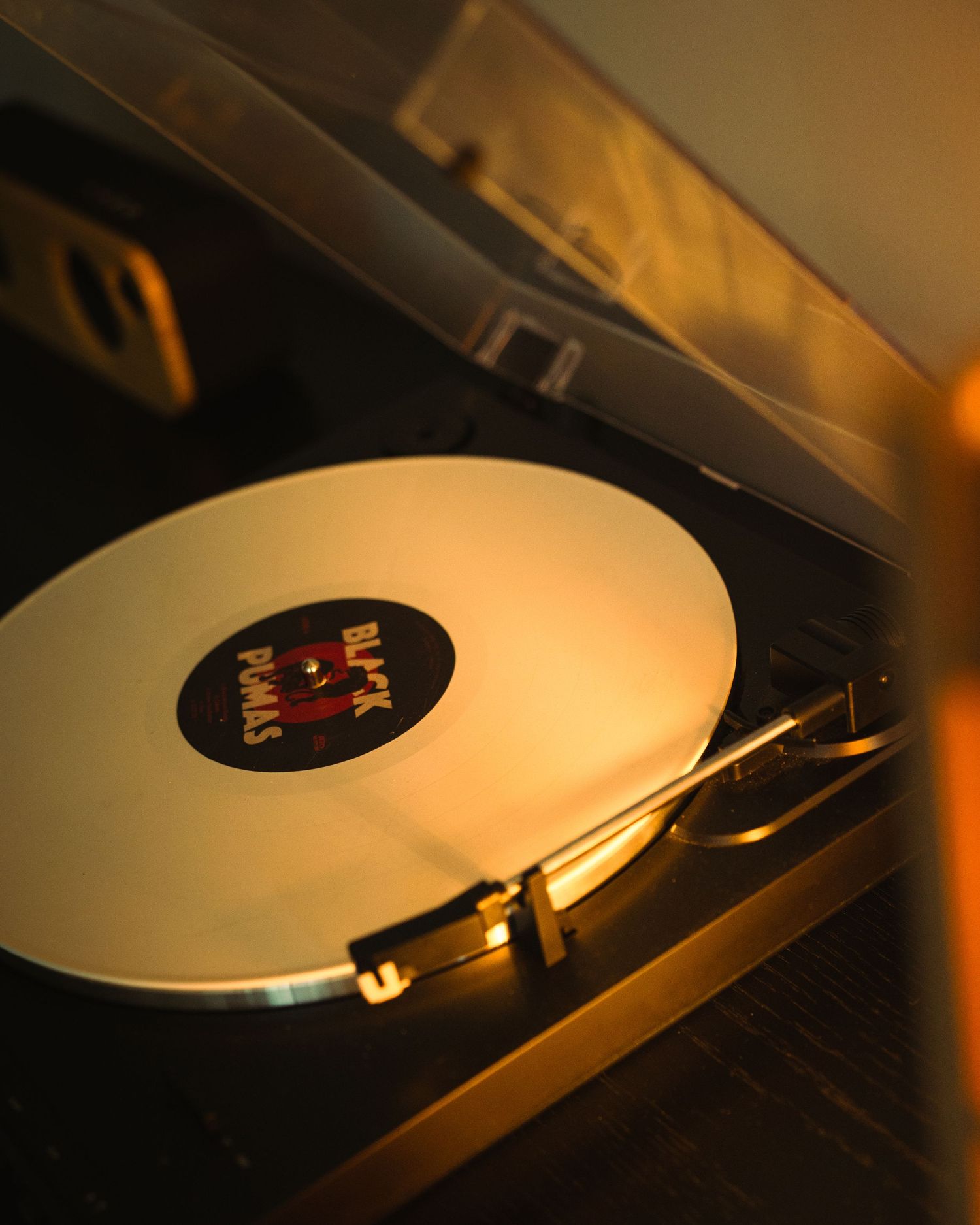 A Black Pumas vinyl record spinning on a warm golden-lit turntable record player.