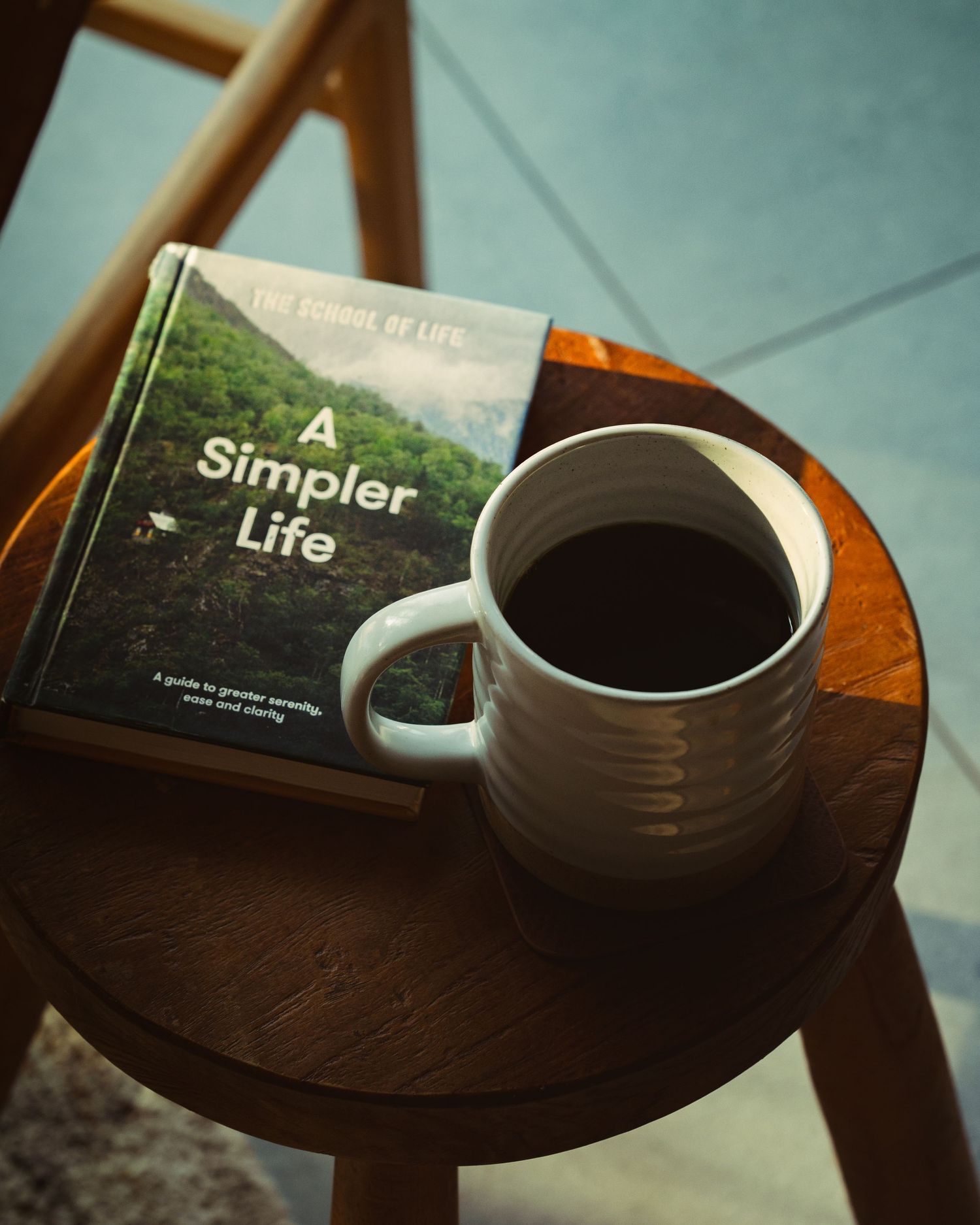 A white ceramic mug of black coffee beside a book titled A Simpler Life on a round wooden side table.
