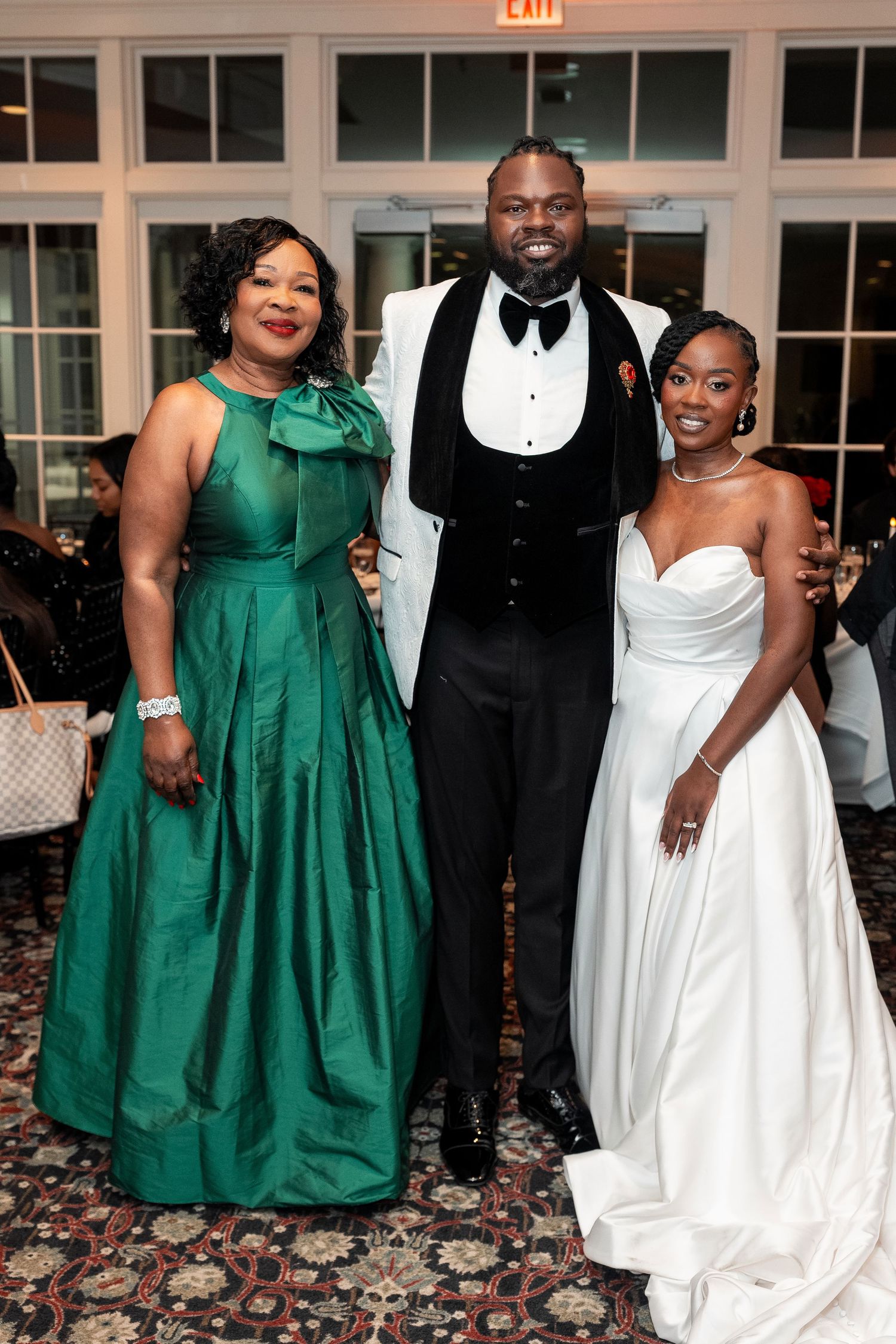 A bride in white gown poses with groom in tuxedo and woman in emerald green gown at wedding reception. Deerfield Golf Club Newark De