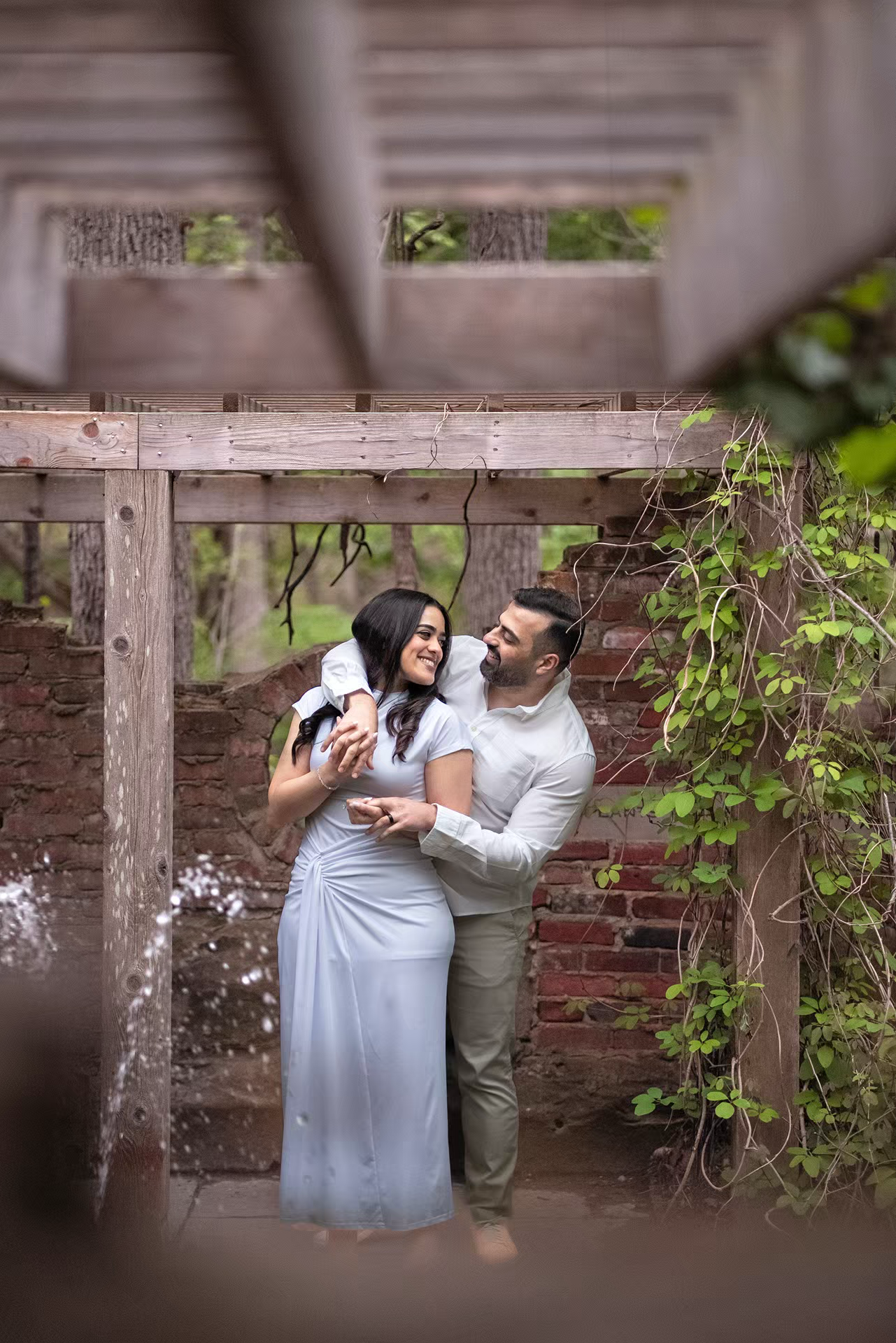 Engagement Photo of couple embraces and laughs together under a rustic wooden pergola at Inniswood Metro Gardens