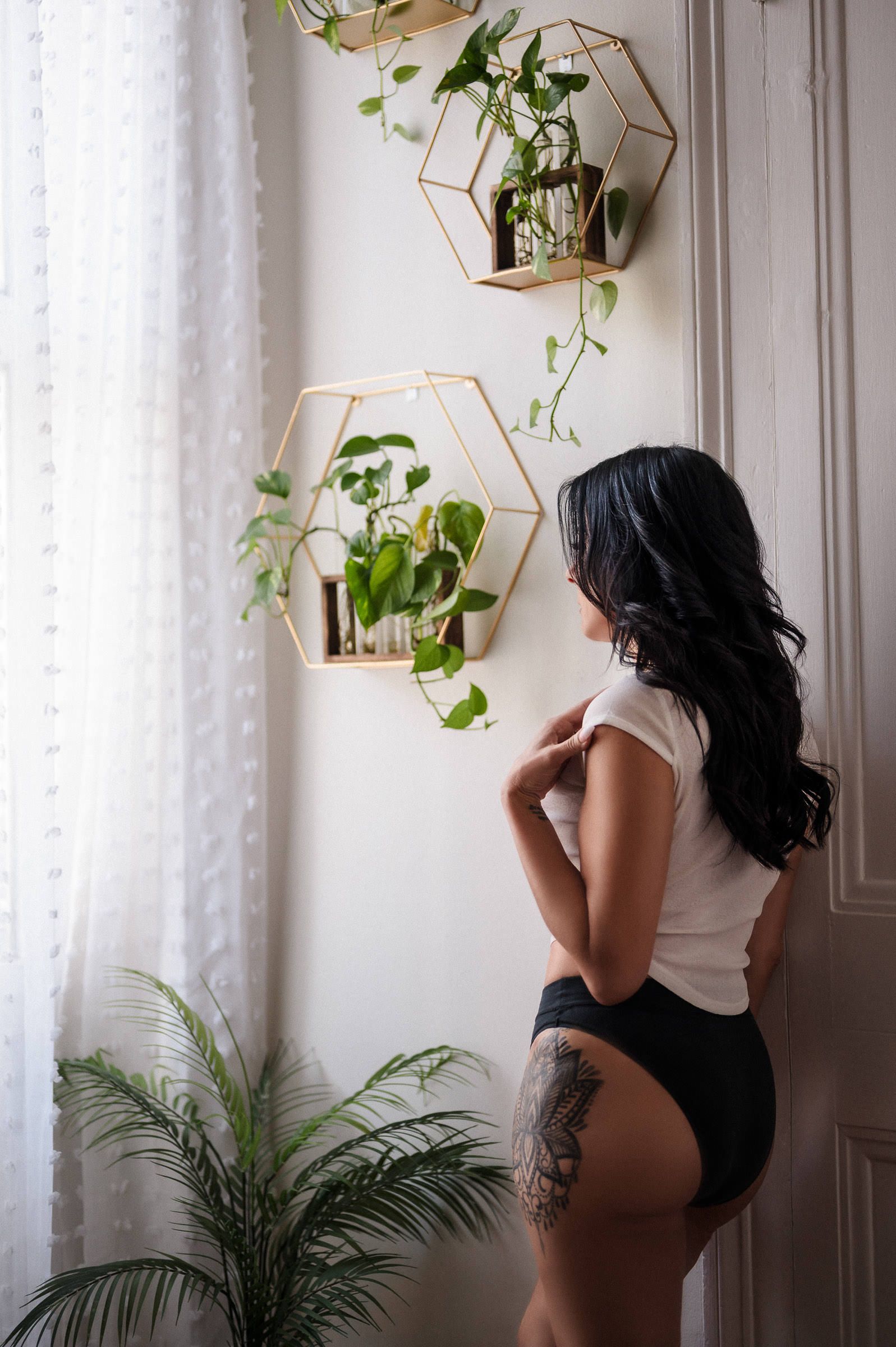 New Orleans Boudoir Photography - Woman with tattoo in white top and black bodysuit poses near geometric gold wall planters.