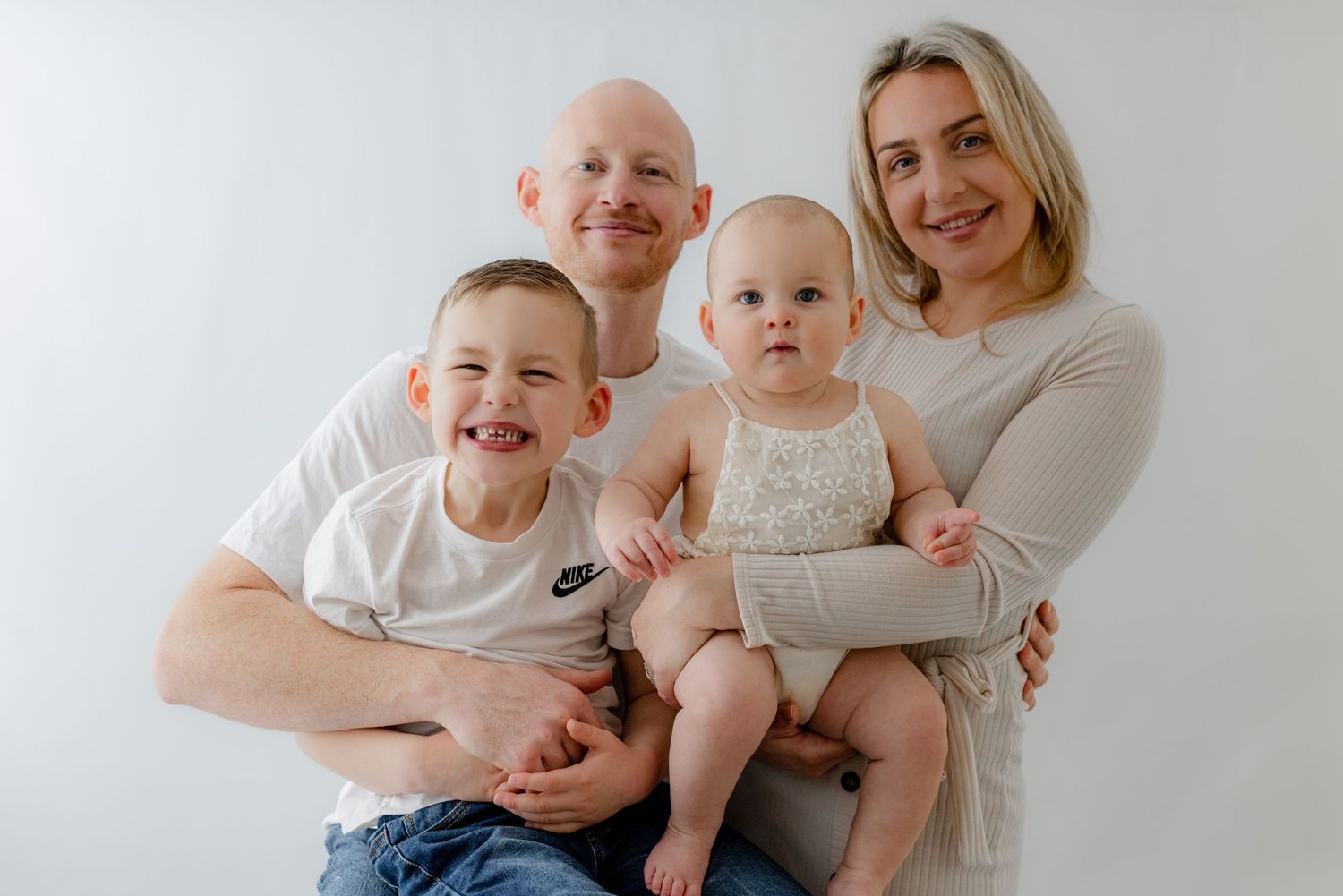 Family of four posing for a studio portrait, parents holding two young children against a white background.