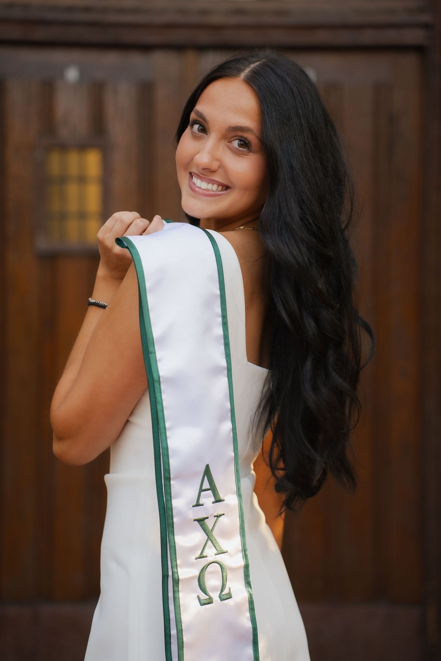 Smiling young woman in white mini dress holding a pink stethoscope, posing outdoors near brick building.