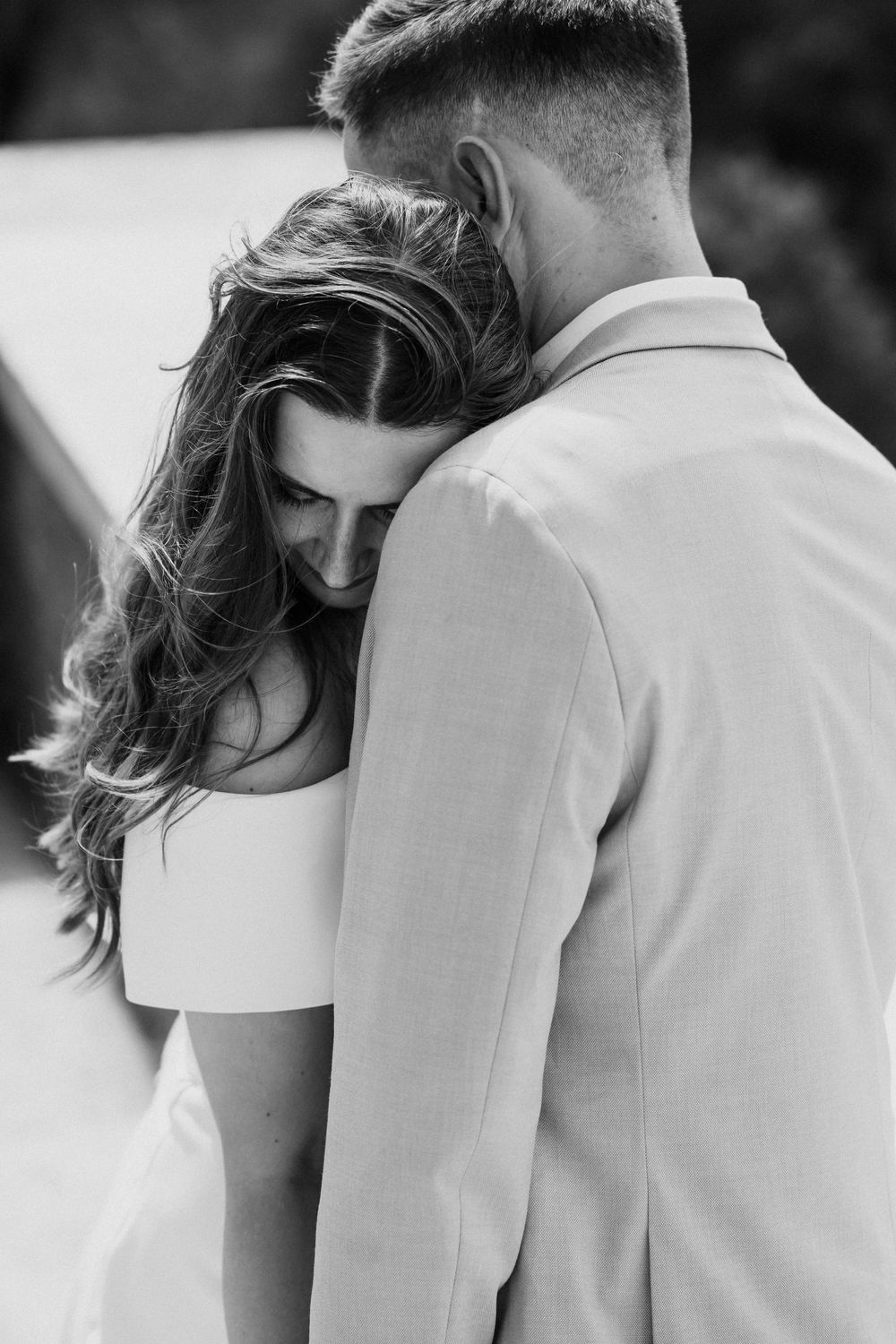Black and white photo of bride leaning head on grooms shoulder in tender romantic wedding moment.