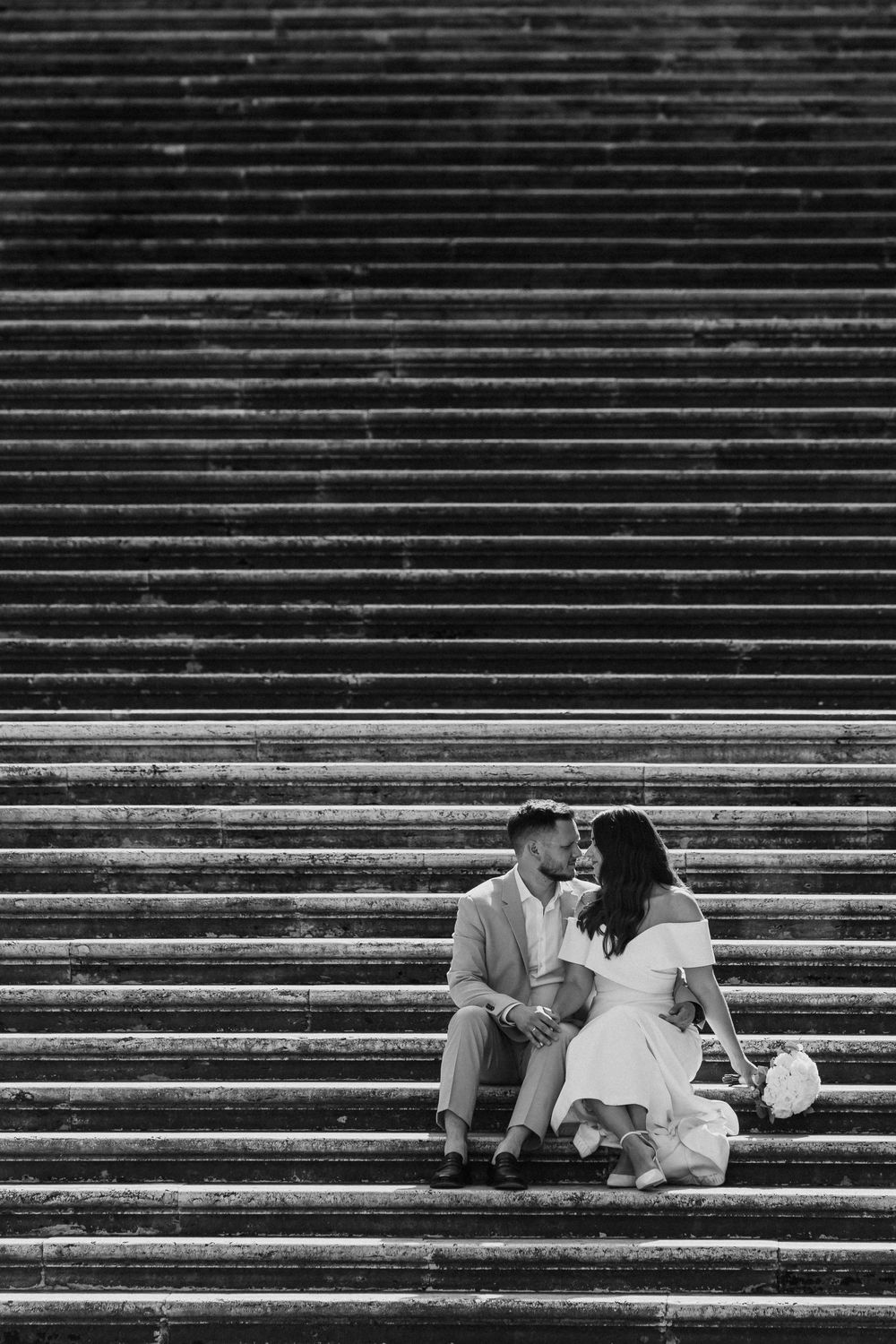Black and white photo of a couple in wedding attire sitting on the Spanish Steps in Rome, sharing an intimate moment.