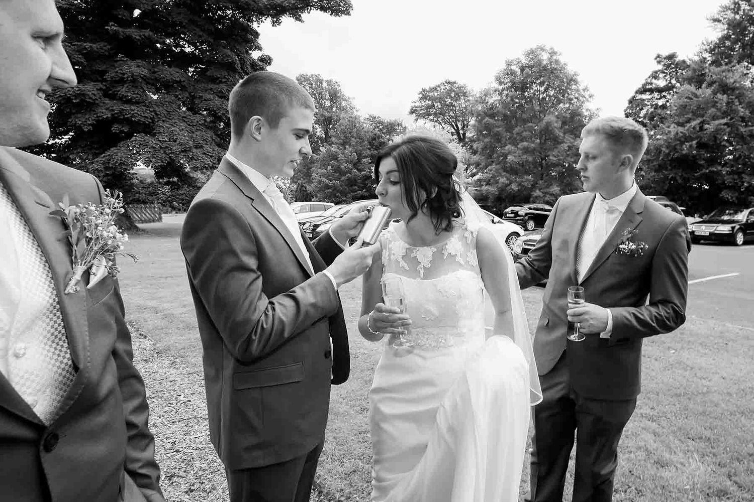 Black and white wedding photo of bride and groom sharing a sneaky nip of whisky before sitting down to the wedding reception at Greenhill.