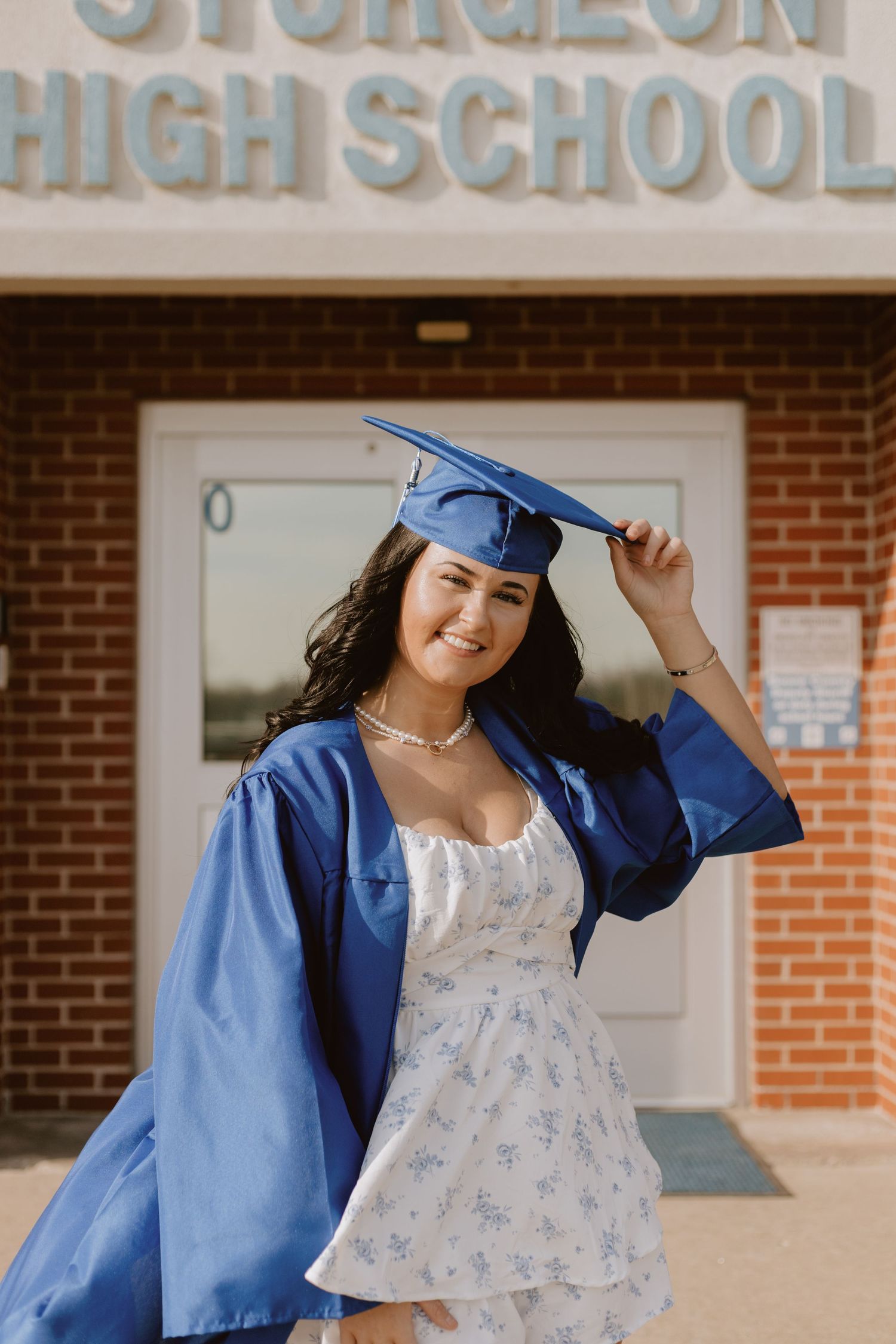 Smiling graduate in blue cap and gown posing in front of Sturgeon High School entrance.