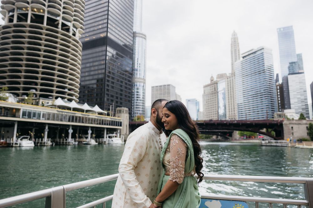 Indian Couple embracing on Chicago Riverwalk with stunning city skyline and skyscrapers in background on cloudy day.