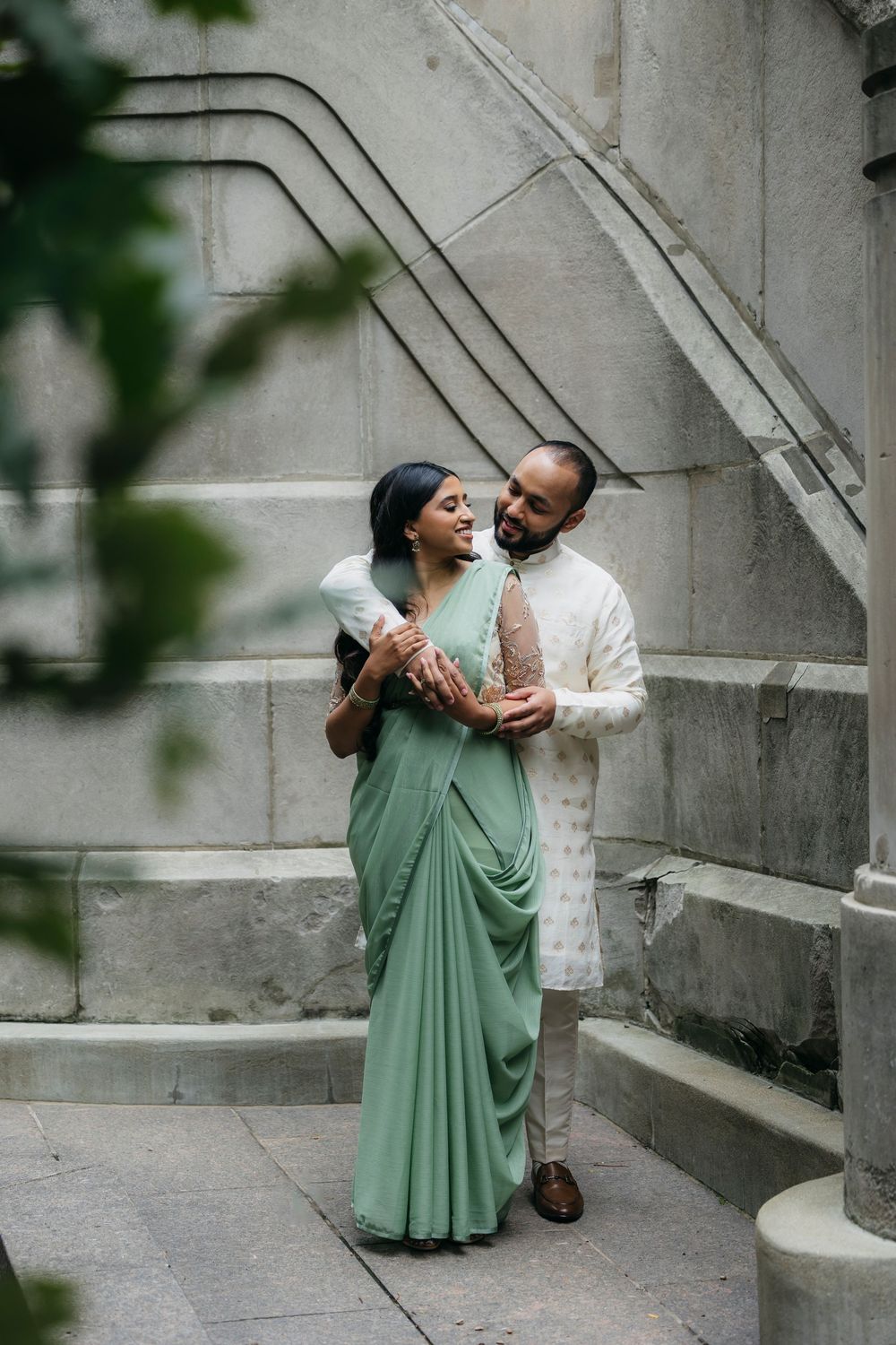 Couple in traditional Indian attire, woman in green saree and man in white kurta, embracing near stone steps at Chicago river walk