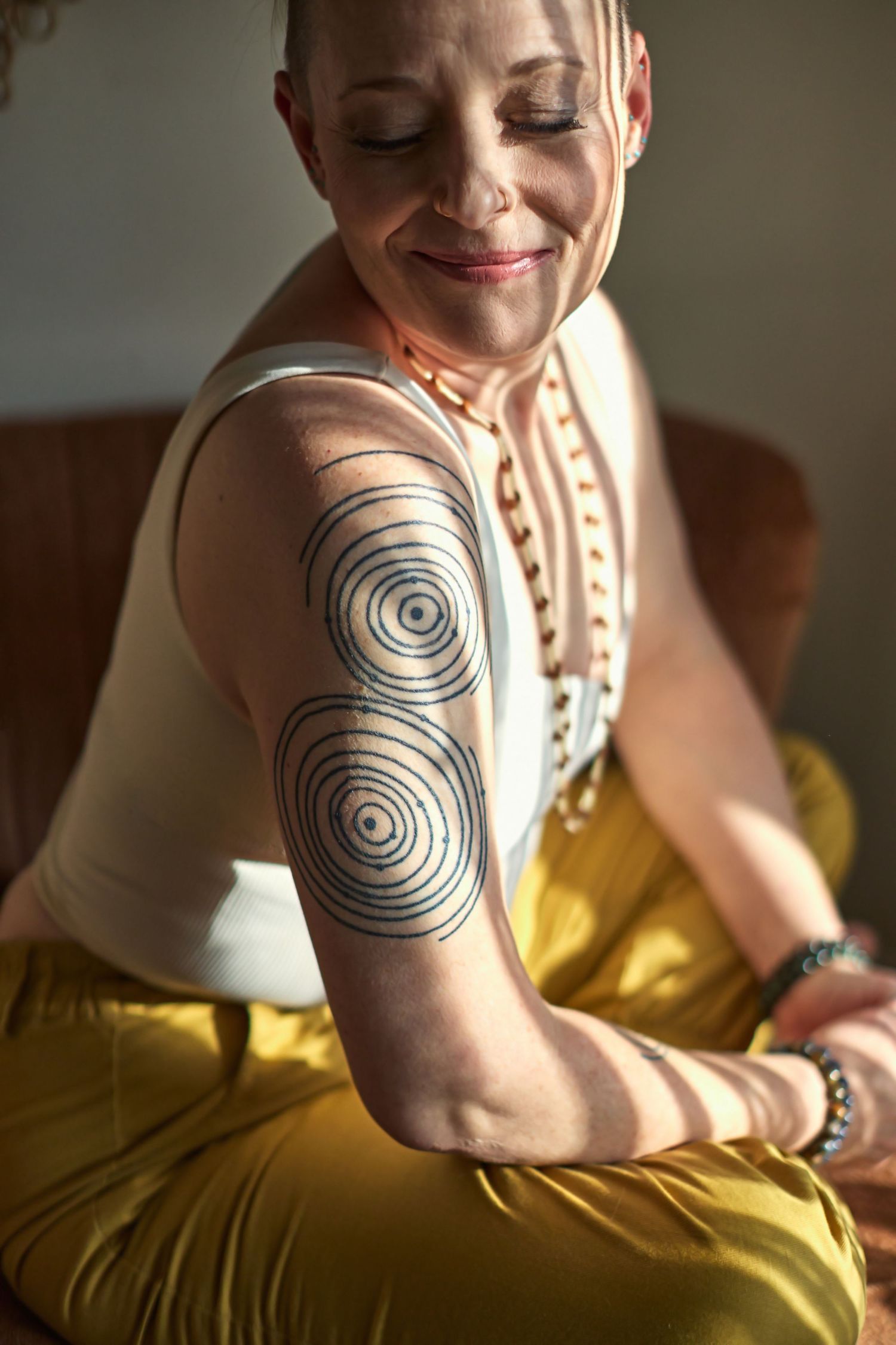 Person with spiral circle tattoos on arm wearing white top and yellow pants in sunlight.