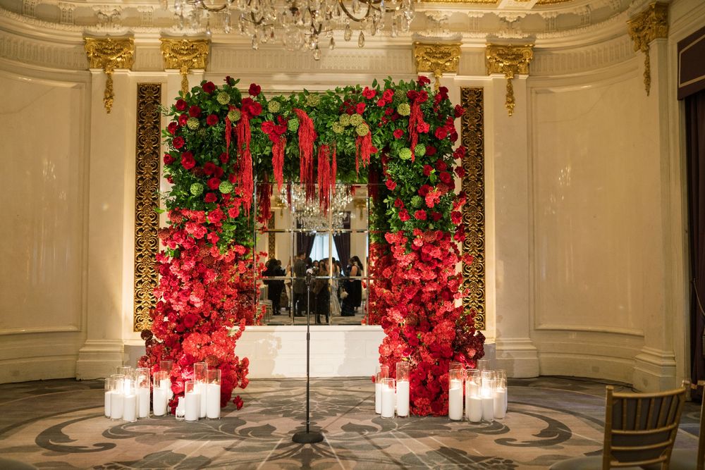 Elegant floral arch with red roses and greenery flanked by candles in a grand ballroom setting.