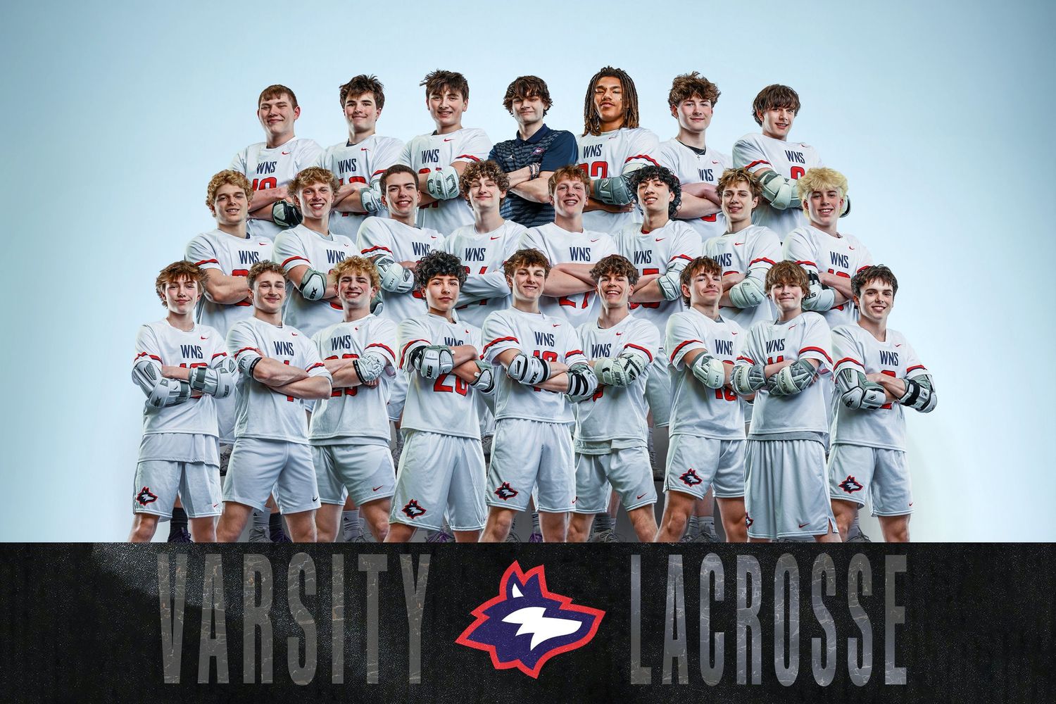 Varsity lacrosse team photo featuring young male players in white uniforms holding helmets with a bold team logo graphic.
