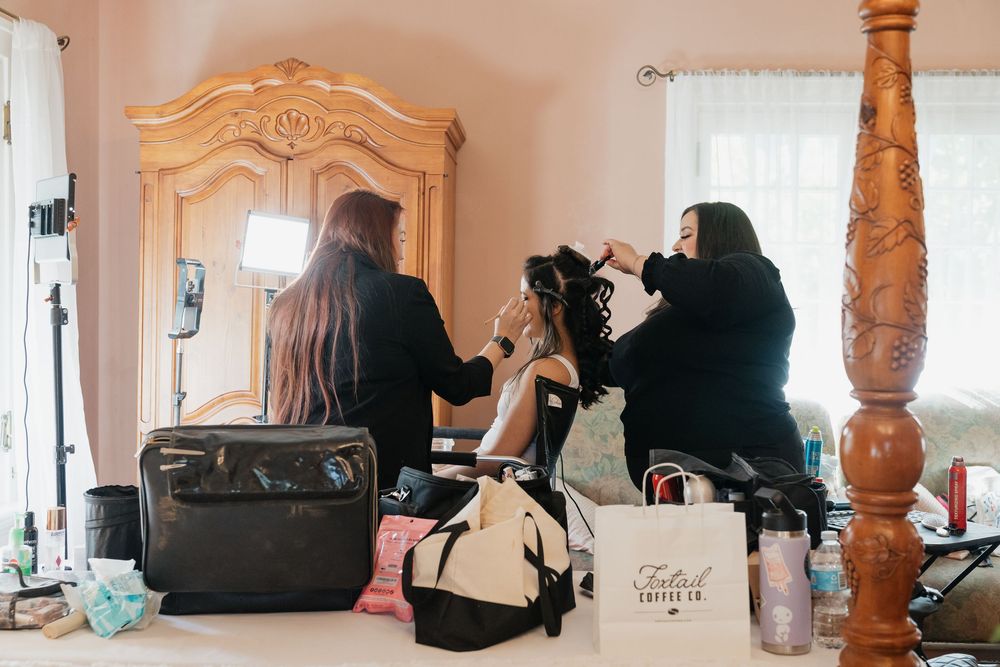 Two stylists prepare a bride with hair and makeup in a elegantly furnished bridal suite before her wedding.