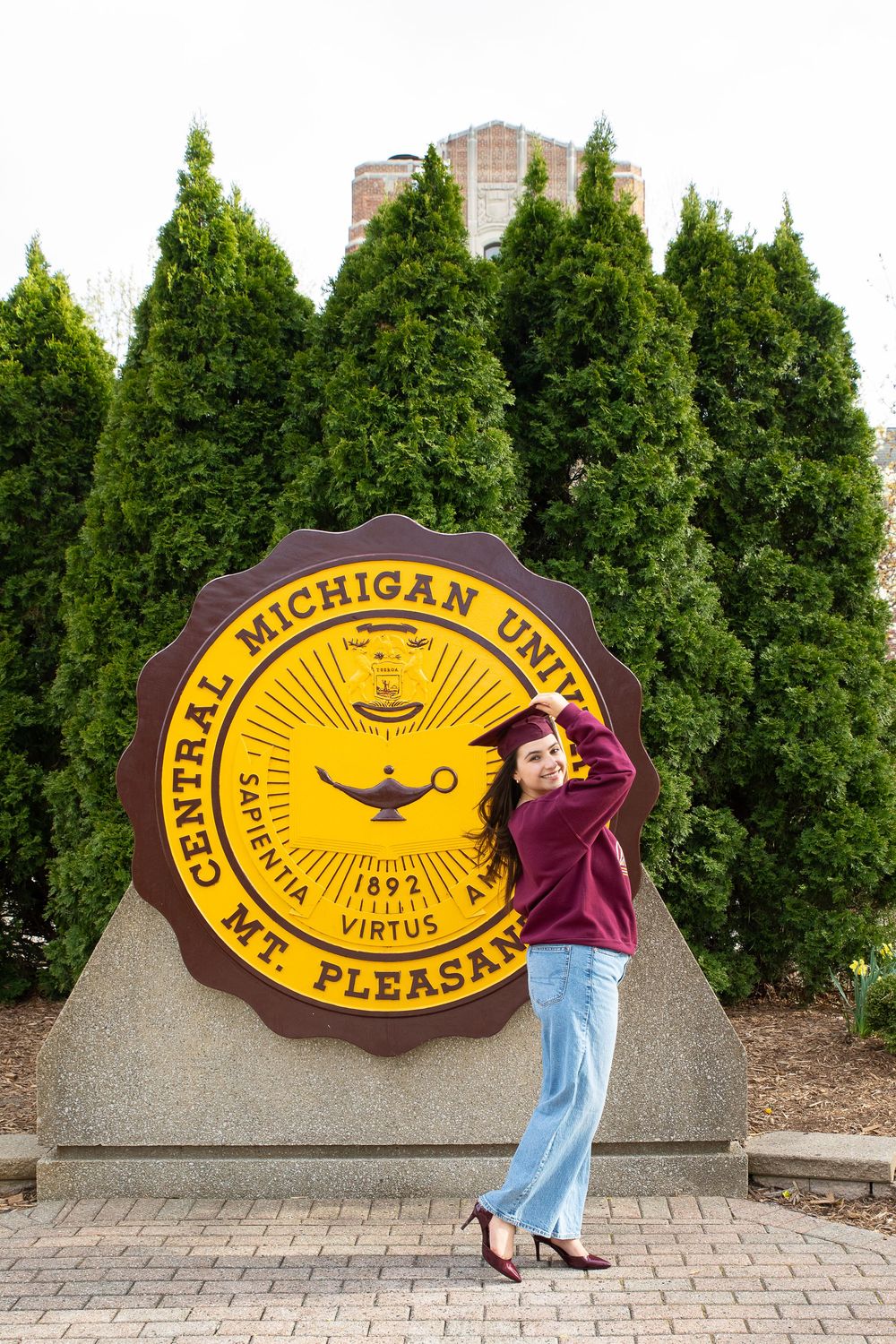 Female student poses proudly in front of Central Michigan University seal monument in Mt. Pleasant campus.