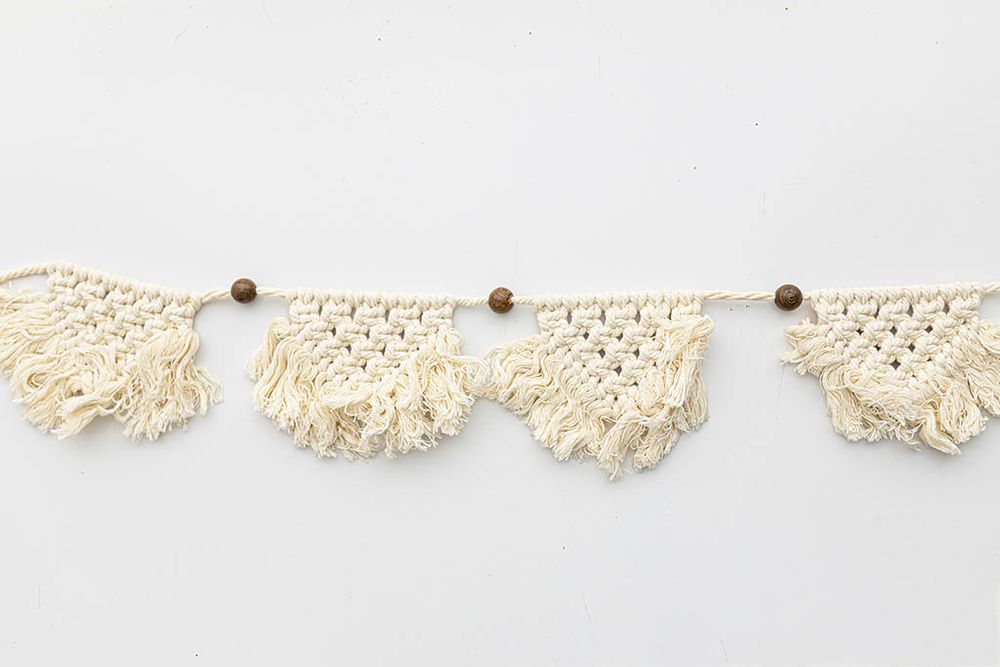 Handmade cream macrame fringe bunting banner with wooden beads on white background.