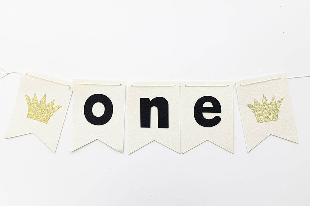 White pennant ONE birthday banner with gold glitter crowns for first birthday party.