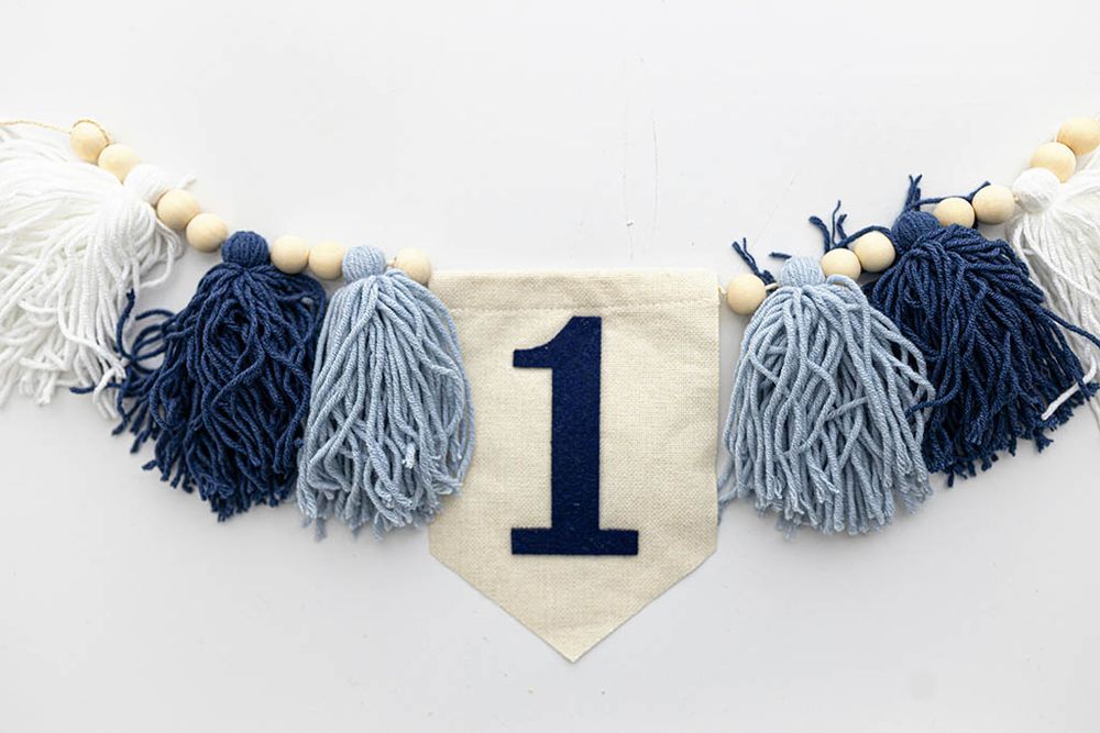 Navy blue tassel and wooden bead garland with number 1 pennant banner. Baby's first birthday photos.