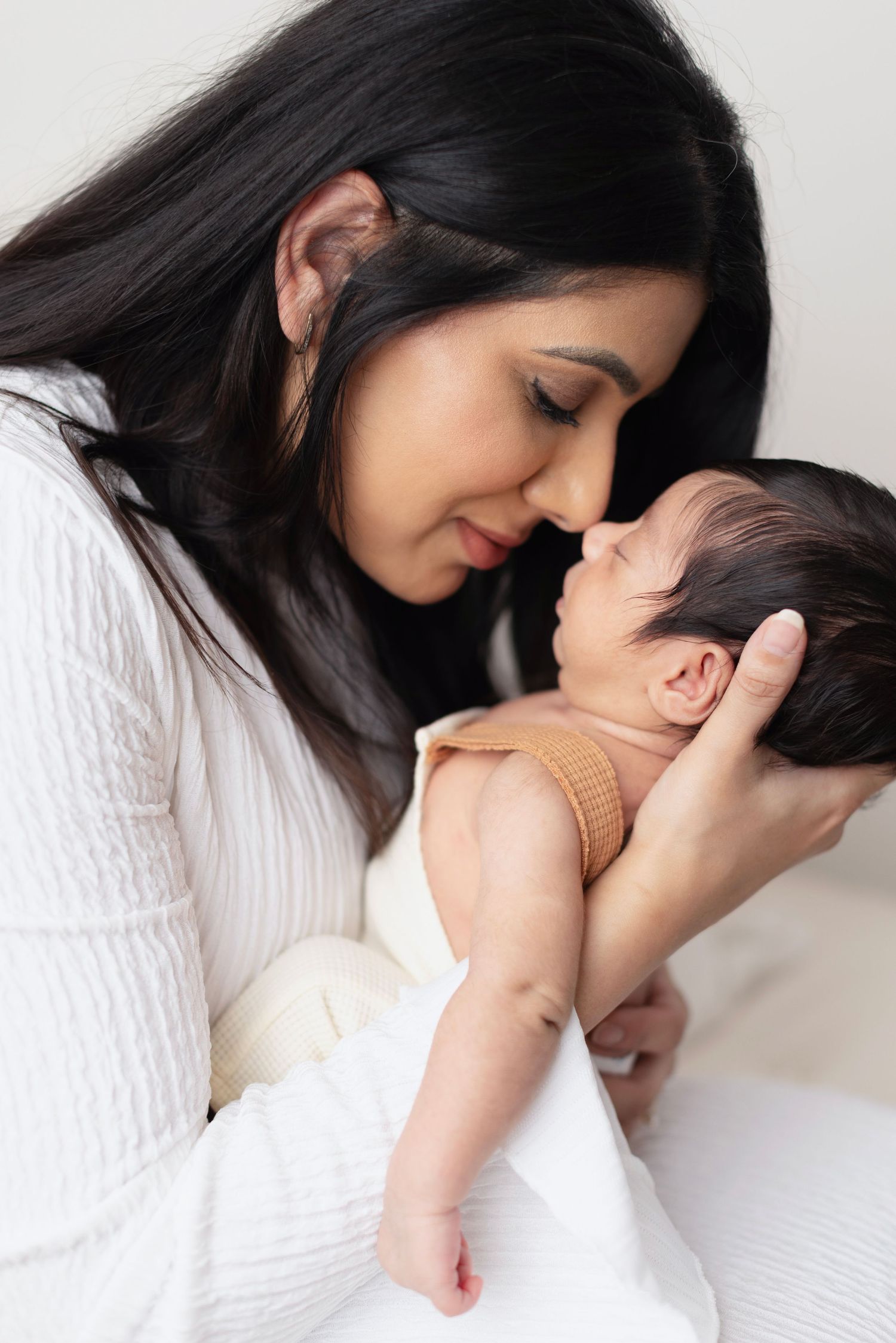 A mother tenderly touches noses with her newborn baby, cradling the infant gently in her arms. Elizabeth Lang Surrey