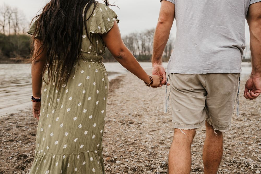 couple holds hand during engagement photos in cincinnati as they walk along the river