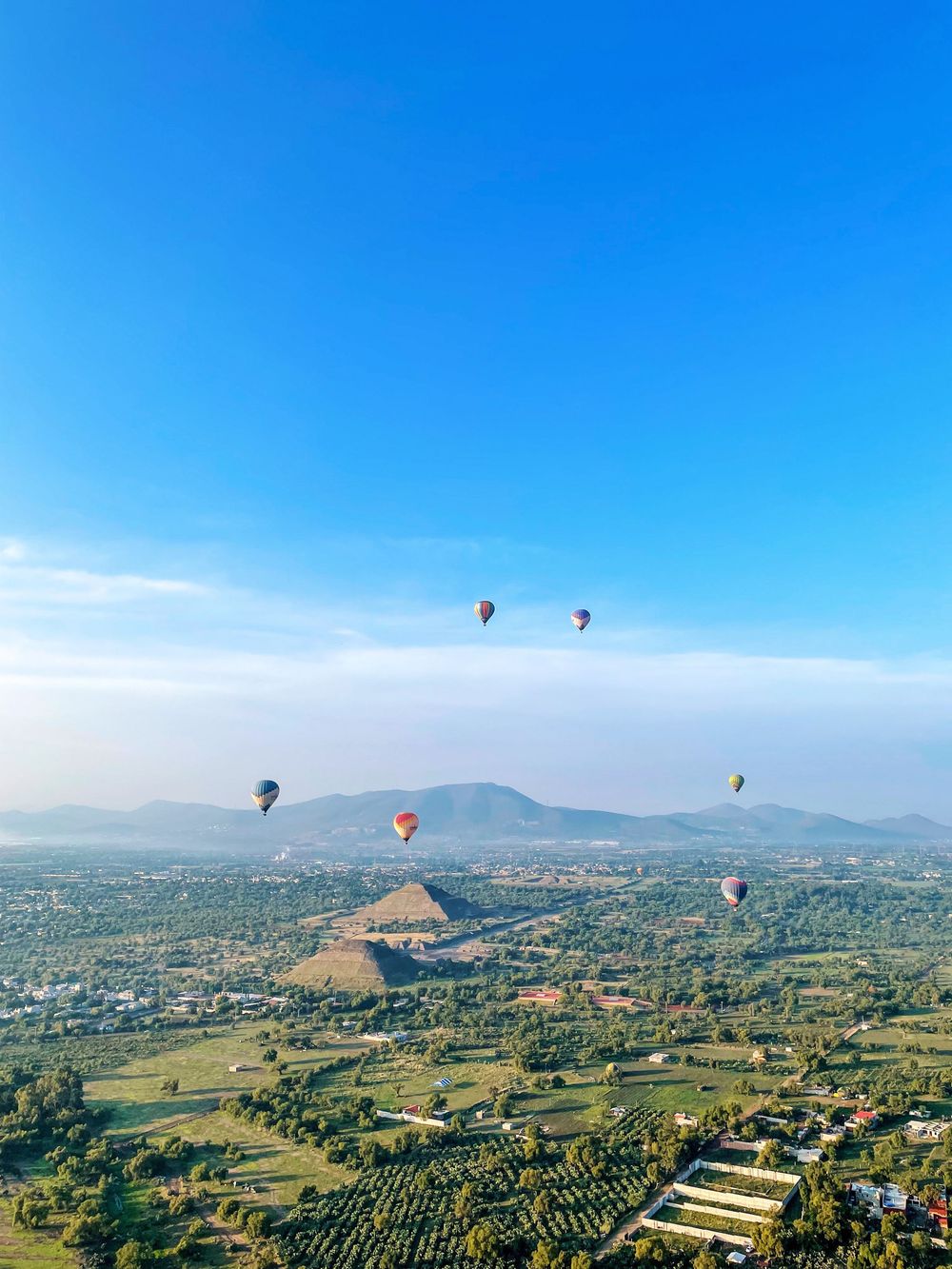 Hot air balloons floating over ancient Teotihuacan pyramids under a vivid blue sky.