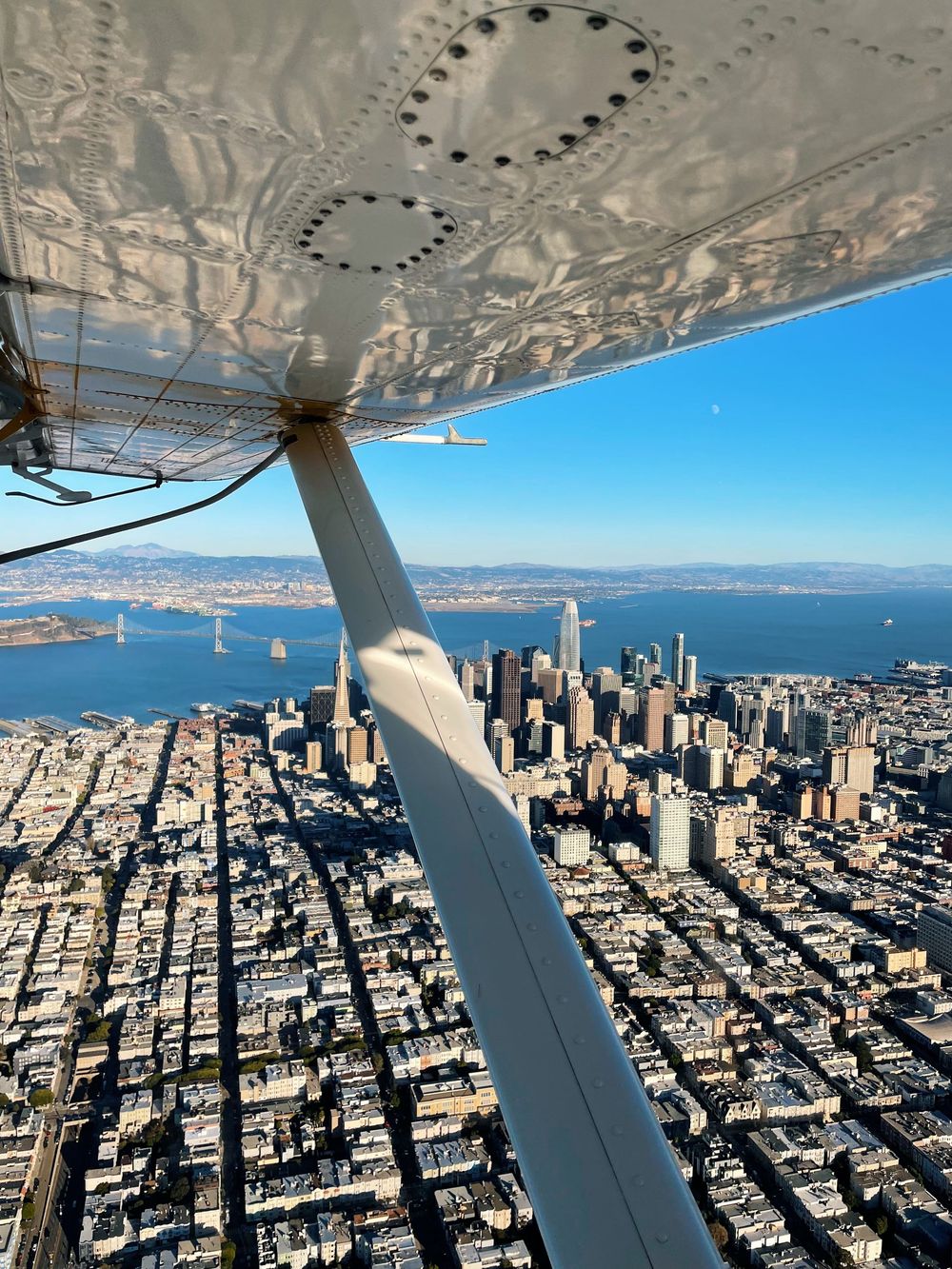 Aerial view of San Francisco skyline and Bay Bridge from a small aircraft wing over the city grid.