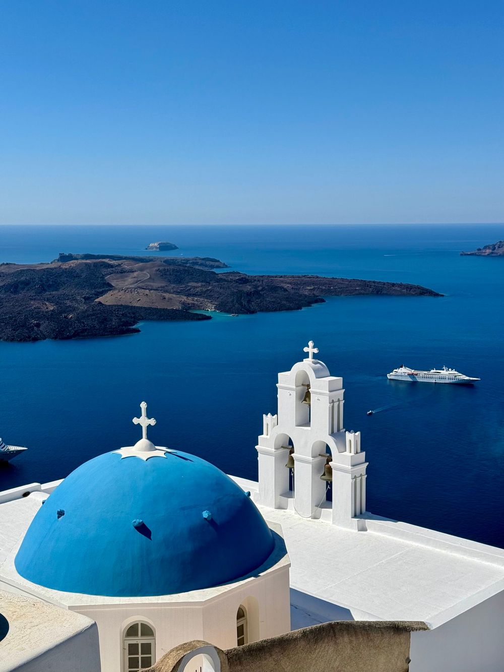 Iconic blue domed church with white bell tower overlooking Santorini caldera and deep blue Aegean Sea.