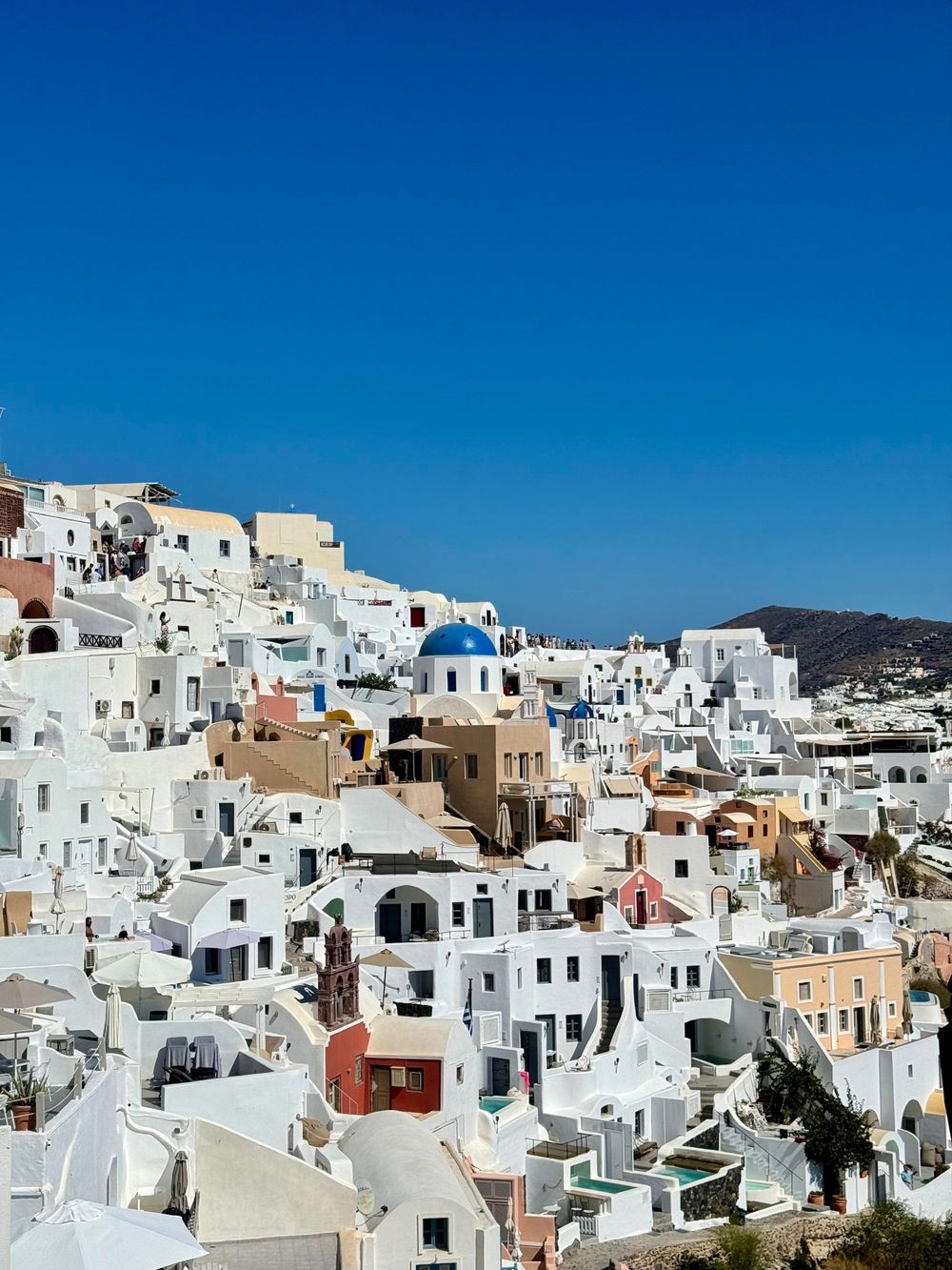 Picturesque Oia village in Santorini with white cubic buildings blue domed church and clear blue sky.