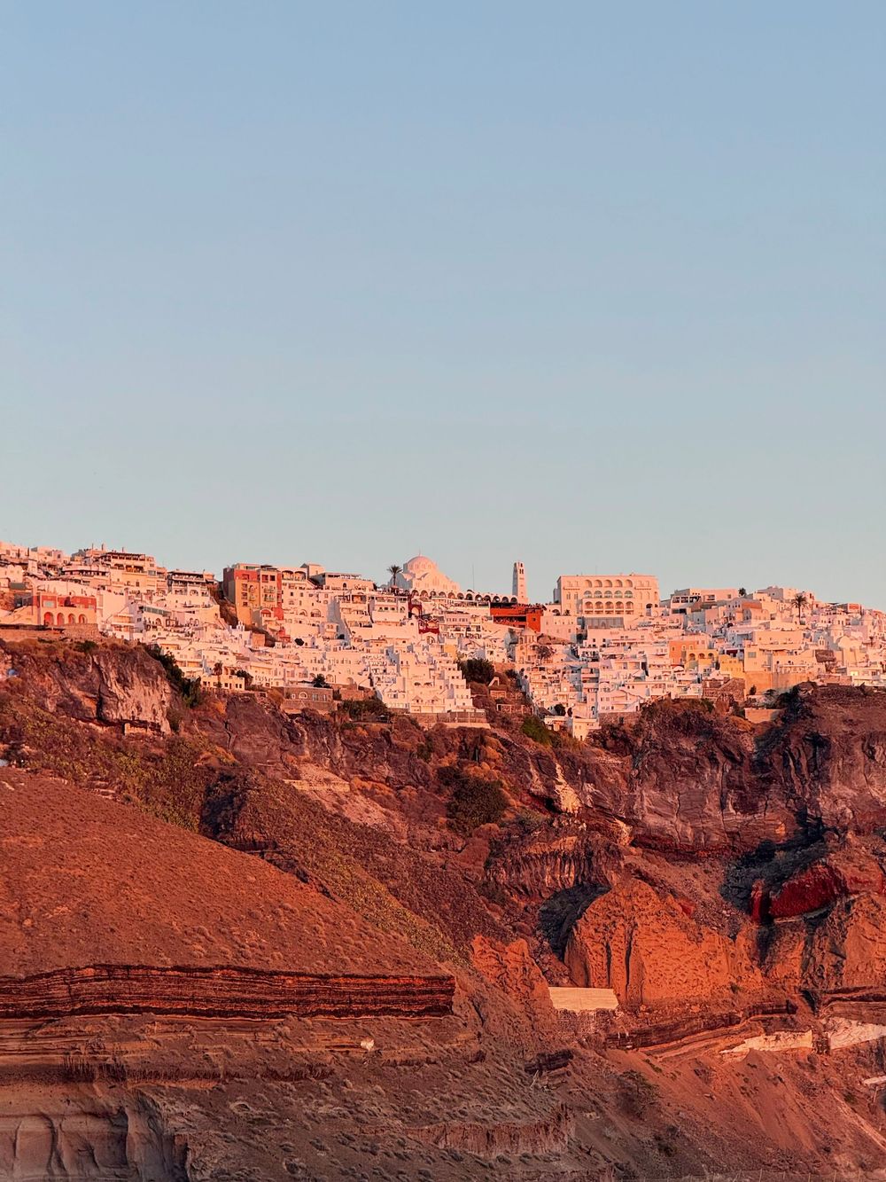 Golden hour light illuminating white buildings of Fira Santorini perched dramatically on volcanic cliffs.