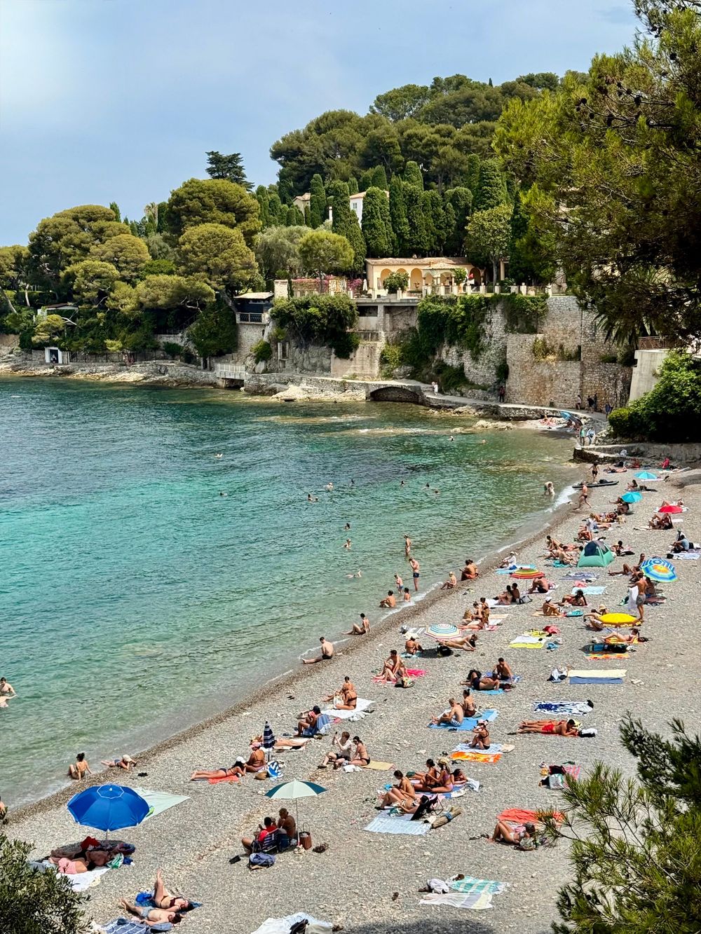 Crowded pebble beach with turquoise water at Paloma Beach near Cap Ferrat on the French Riviera in summer.