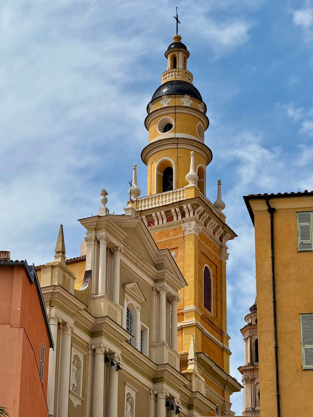 Ornate yellow Baroque bell tower of Saint Michel church rising above colorful buildings in Menton French Riviera.