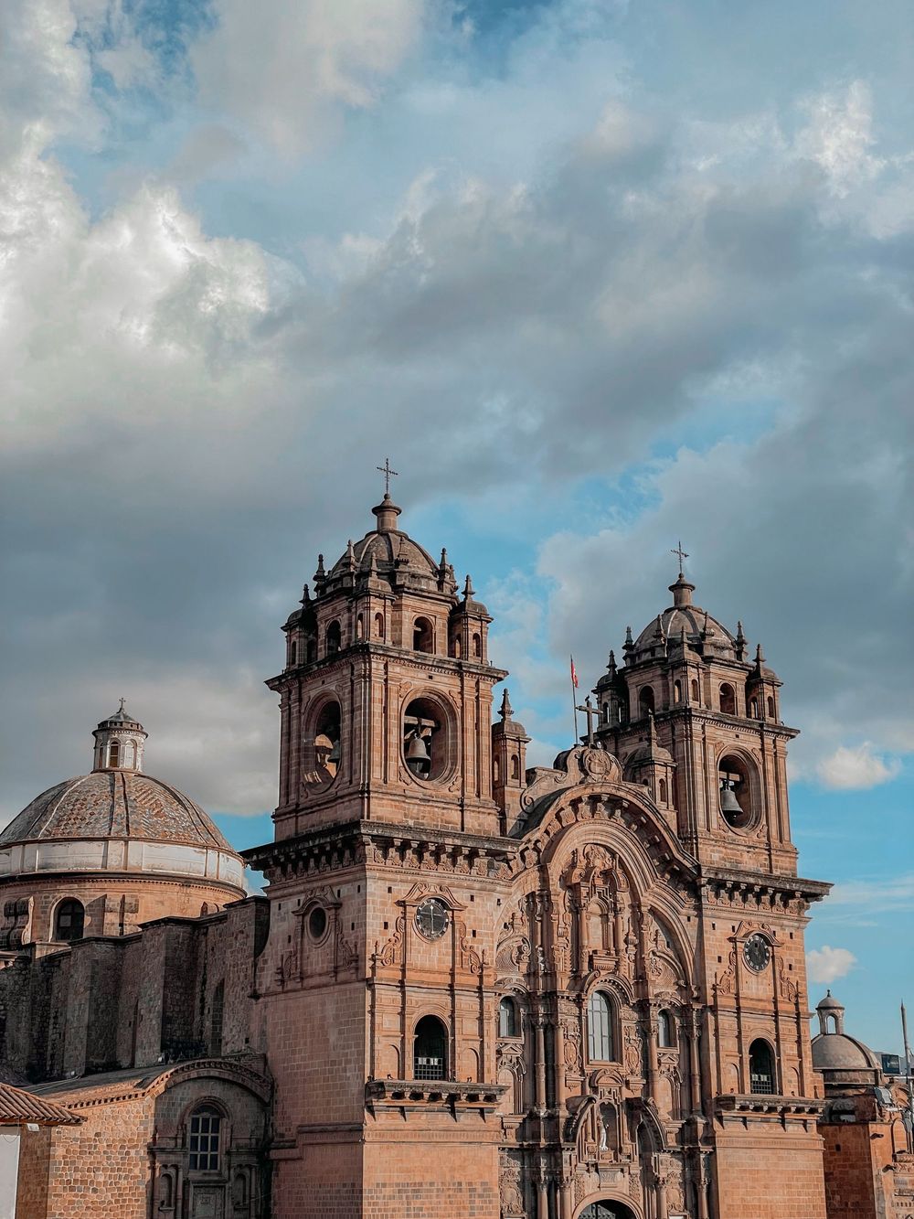 Historic baroque cathedral with twin bell towers and ornate stone facade in Cusco, Peru under cloudy sky.