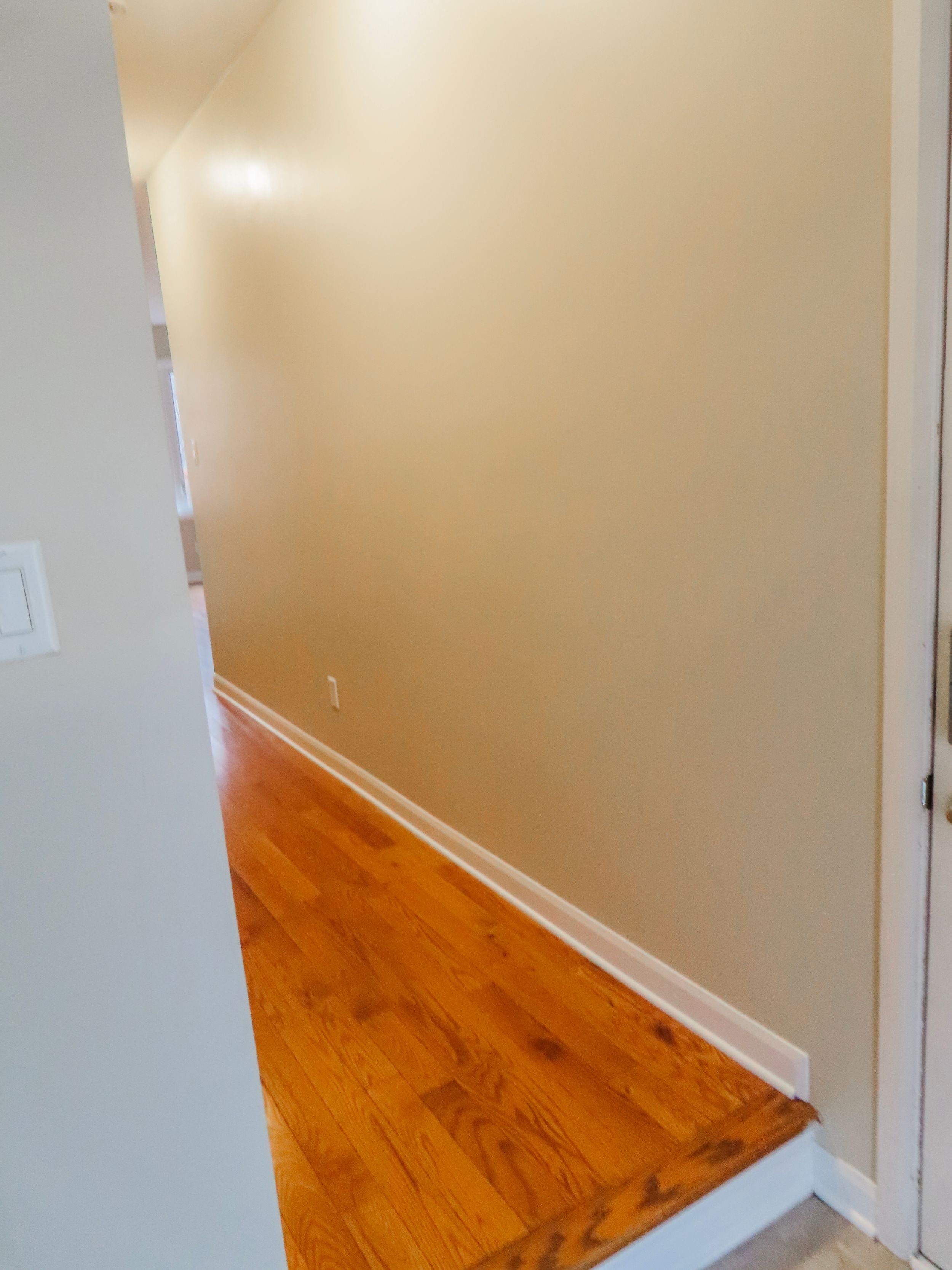 Empty hallway corner with warm hardwood floors and white baseboards in a clean home.