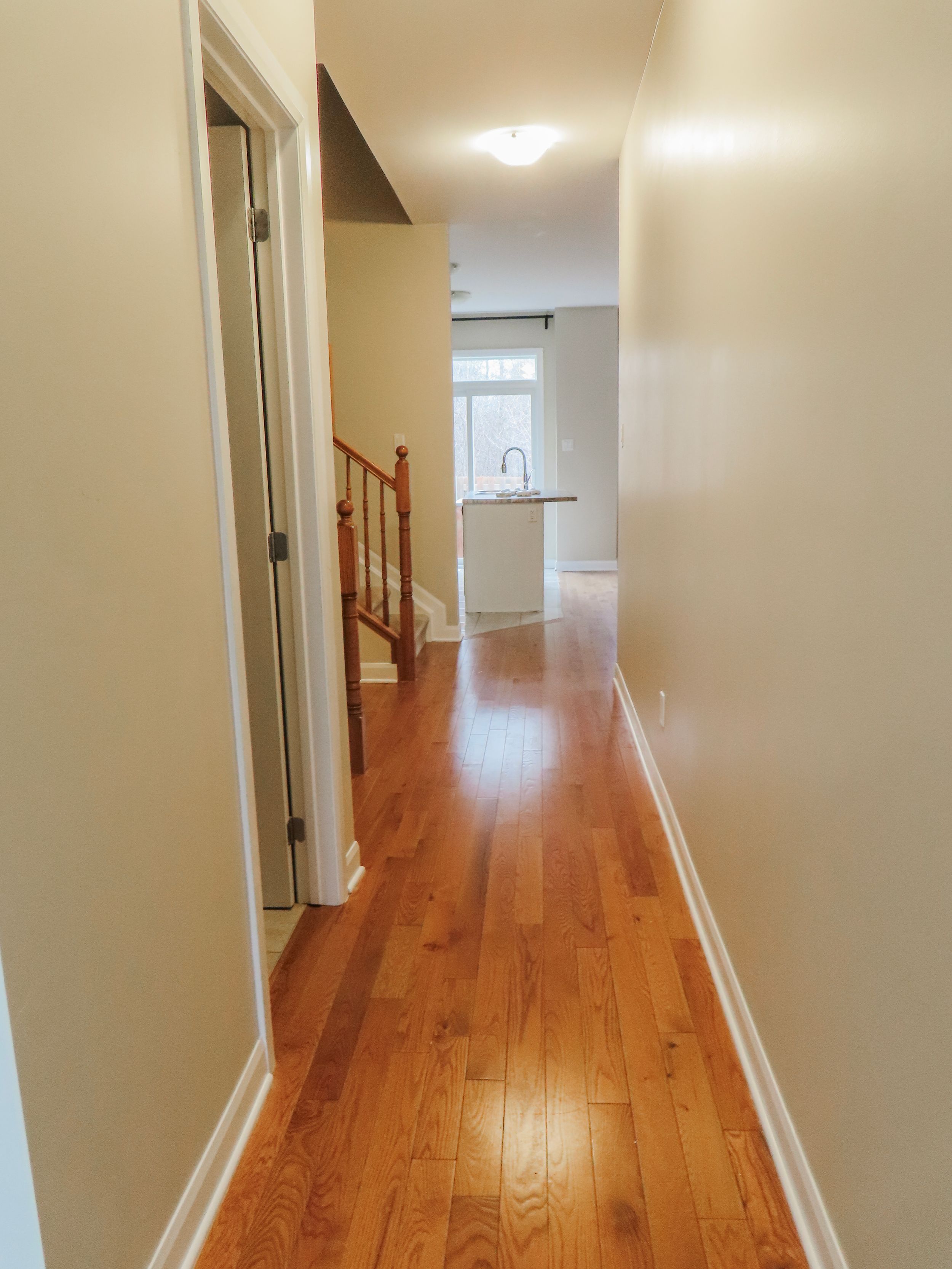 Bright hallway with hardwood floors leading to kitchen with staircase and natural light.