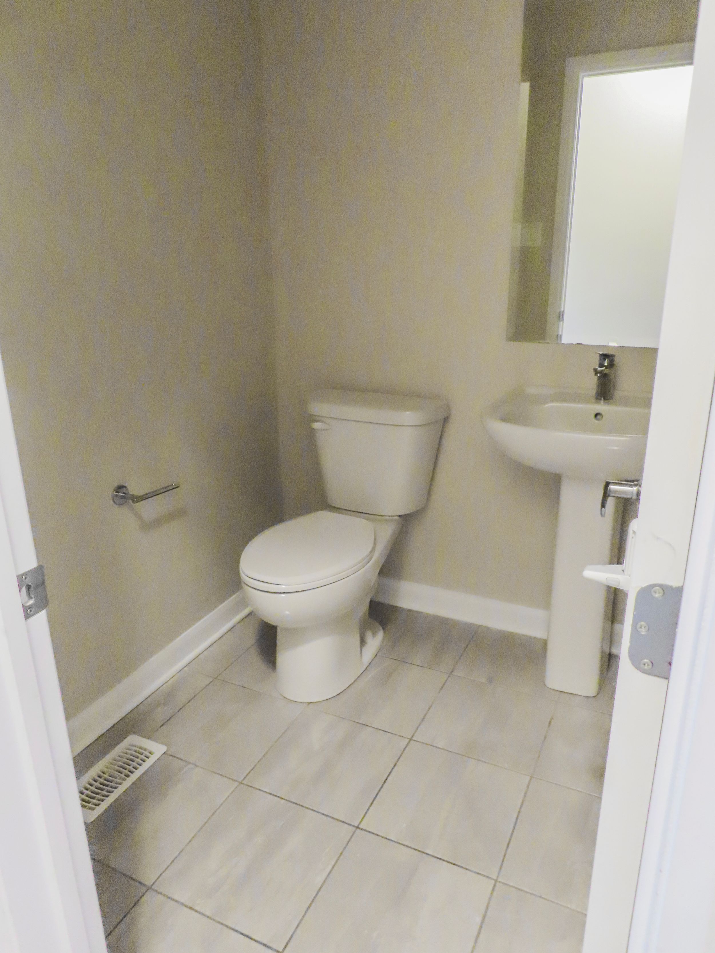 Clean half bathroom with white pedestal sink, toilet, and light tile flooring in a neutral beige interior.