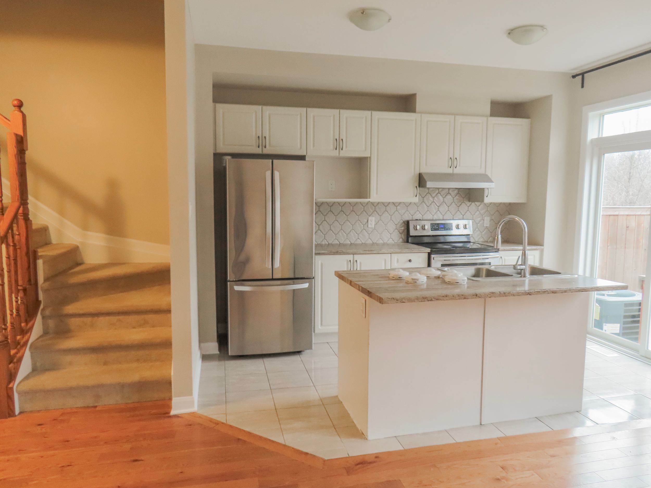 Modern kitchen with white cabinets, stainless steel appliances, granite island, and hardwood floors.