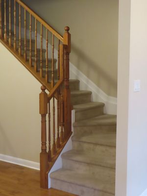Elegant wooden staircase with turned spindles, ball-top newel post, and neutral carpet treads in home interior.