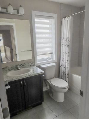 Modern bathroom with granite vanity, white toilet, tiled floors, and shower-tub combo.