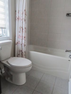 Clean white bathroom with floral shower curtain, bathtub, and toilet on gray tile floor.