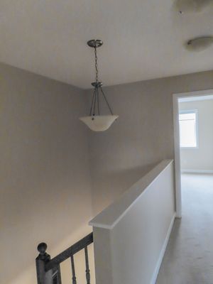 Bright hallway with pendant light fixture, white staircase railing, and neutral gray walls in a modern home.