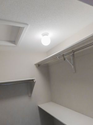 Walk-in closet with white shelving, hanging rod, and ceiling light fixture in a residential home.
