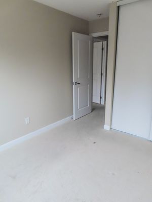 Empty bedroom with neutral carpet, white door, and sliding closet door in a residential home.